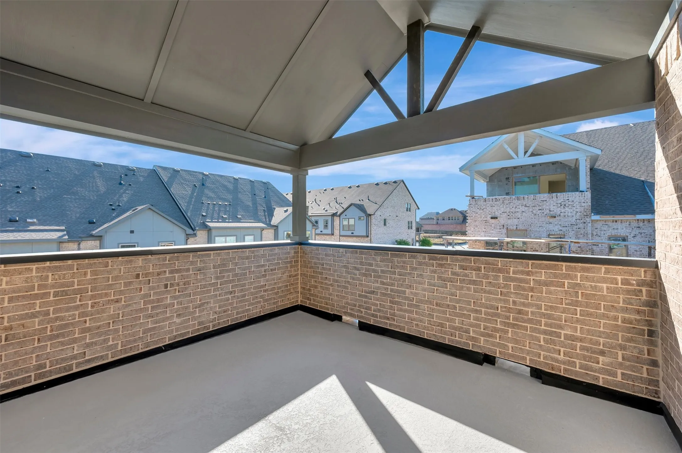 Covered outdoor balcony with a brick half-wall, a durable flooring surface, and exposed structural beams