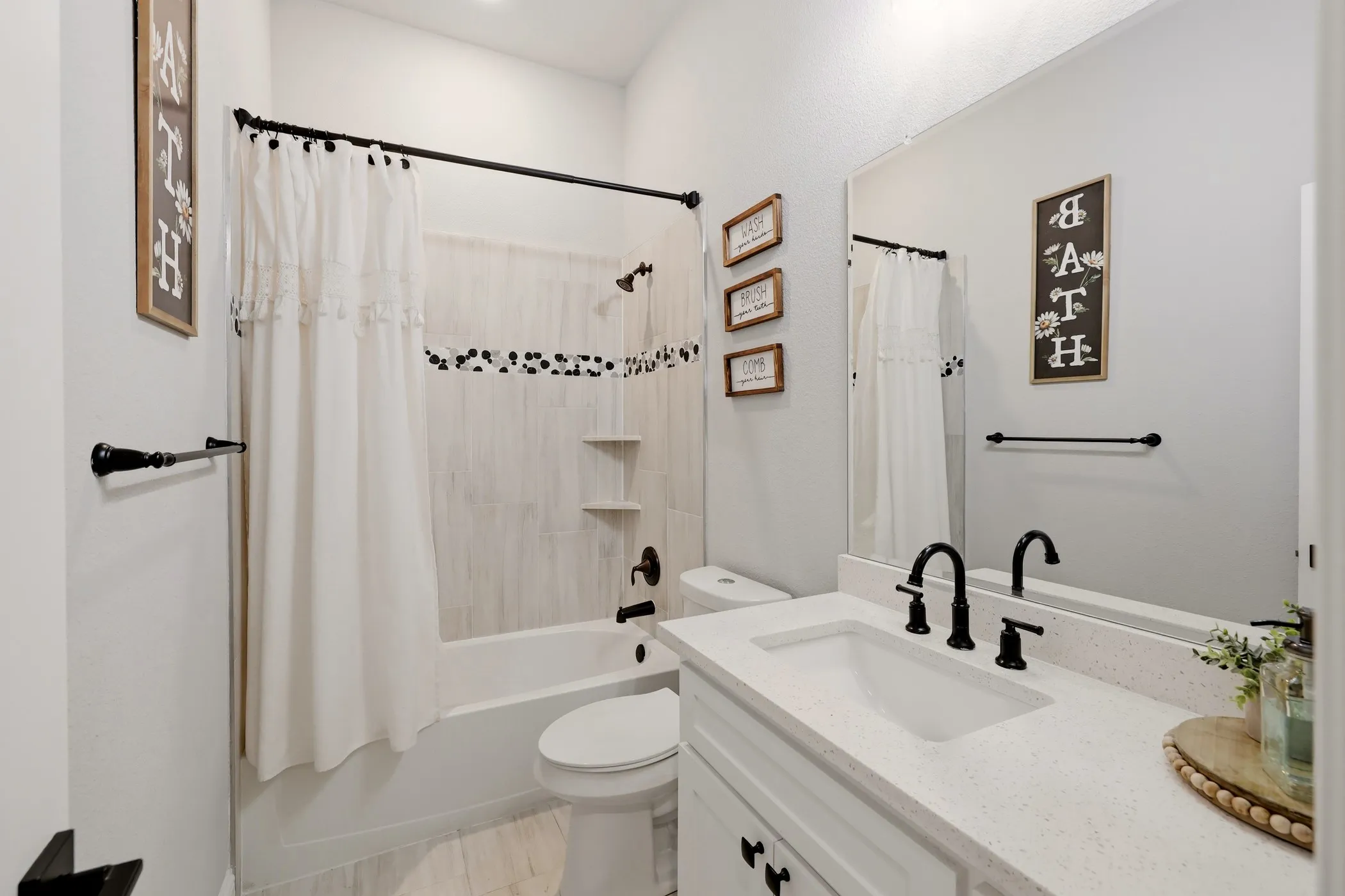 Bathroom featuring a white vanity with an integrated sink and speckle-finish countertop, matte black fixtures, a built-in bathtub with subway tile surround, and wood-finish tile flooring