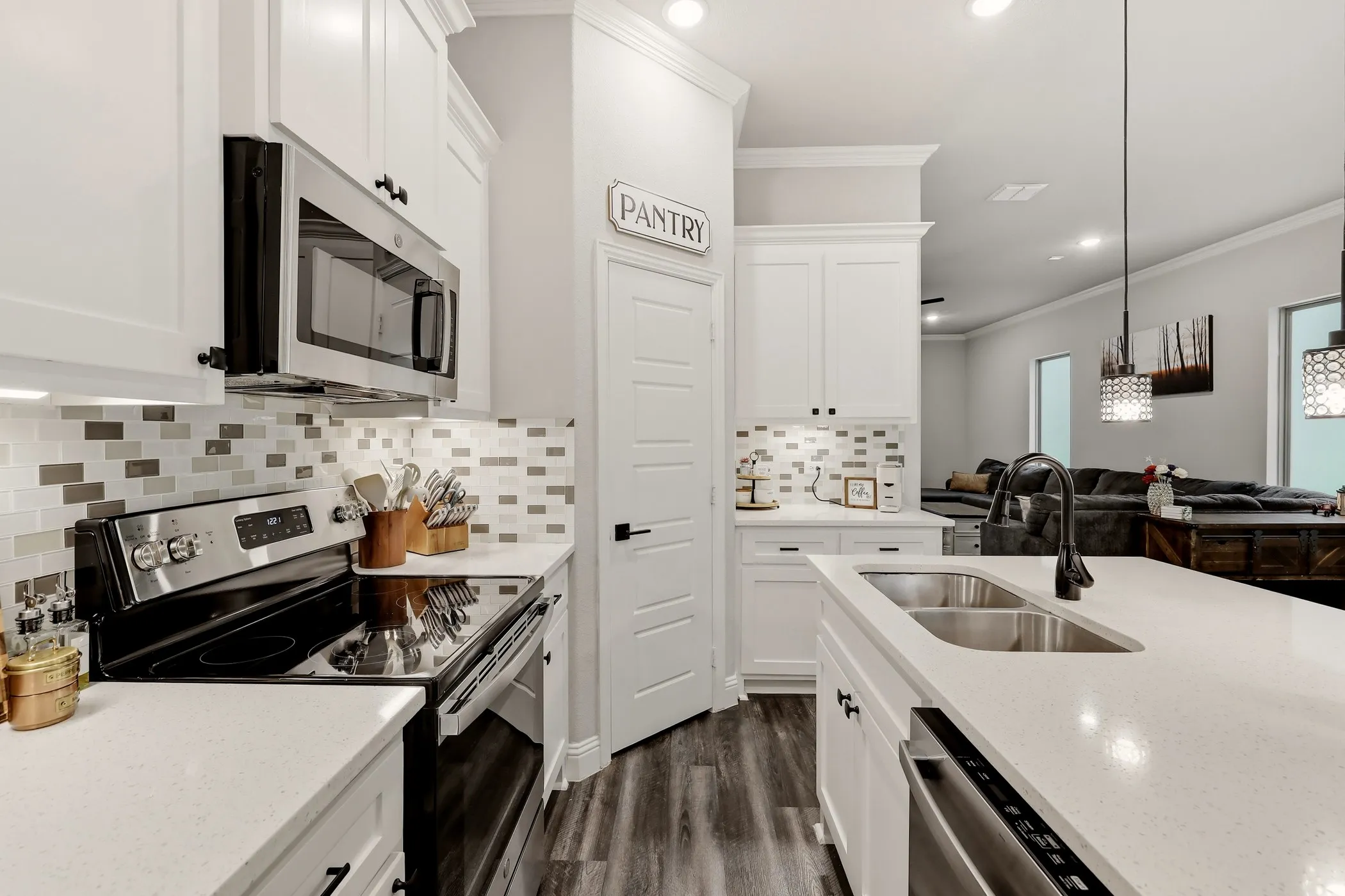 Modern kitchen featuring white shaker cabinetry, stainless steel appliances, a mosaic tile backsplash, wood-finish flooring, and a large island with an undermount double-basin sink