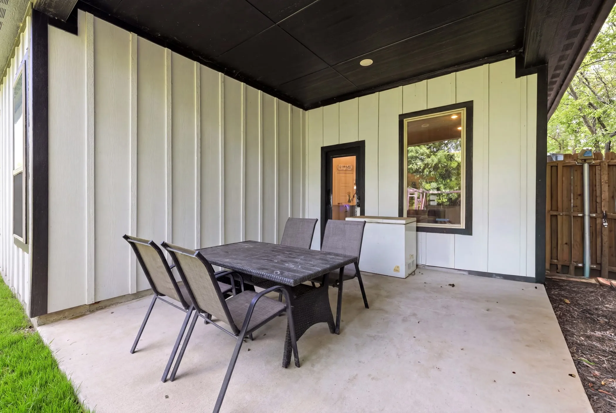 Covered concrete patio featuring board and batten siding with dark trim, a recessed ceiling light, and a wooden privacy fence