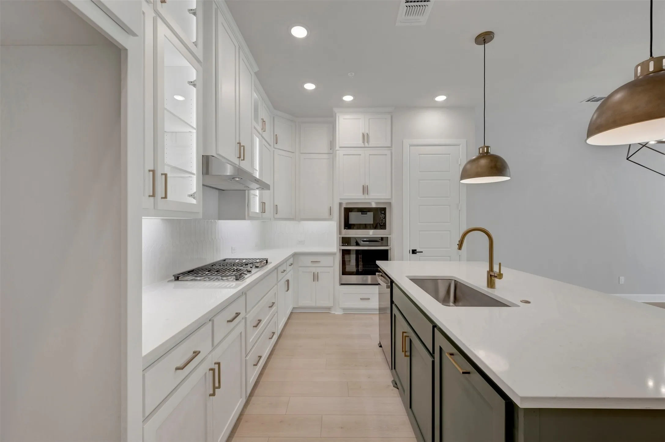 Kitchen featuring white cabinetry with brass hardware, light wood-finish flooring, a kitchen island with an undermount sink and gooseneck faucet, and stainless steel built-in appliances