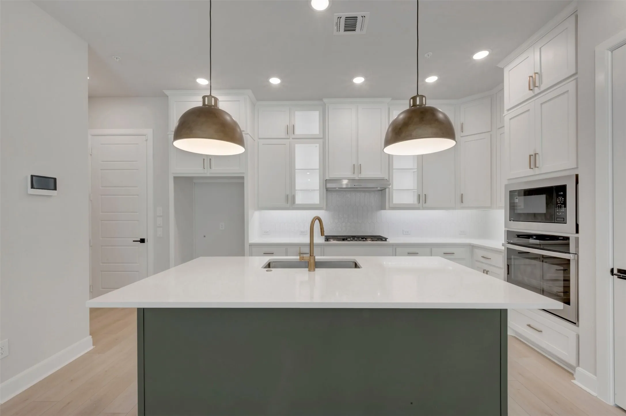 Kitchen featuring a two-tone island with a light-colored countertop, built-in stainless steel appliances, white cabinetry, and wood-finish flooring