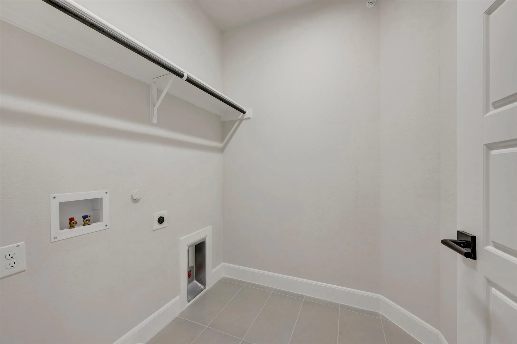 Laundry area featuring a utility hookup, durable tile flooring, and integrated shelving with a hanging rod
