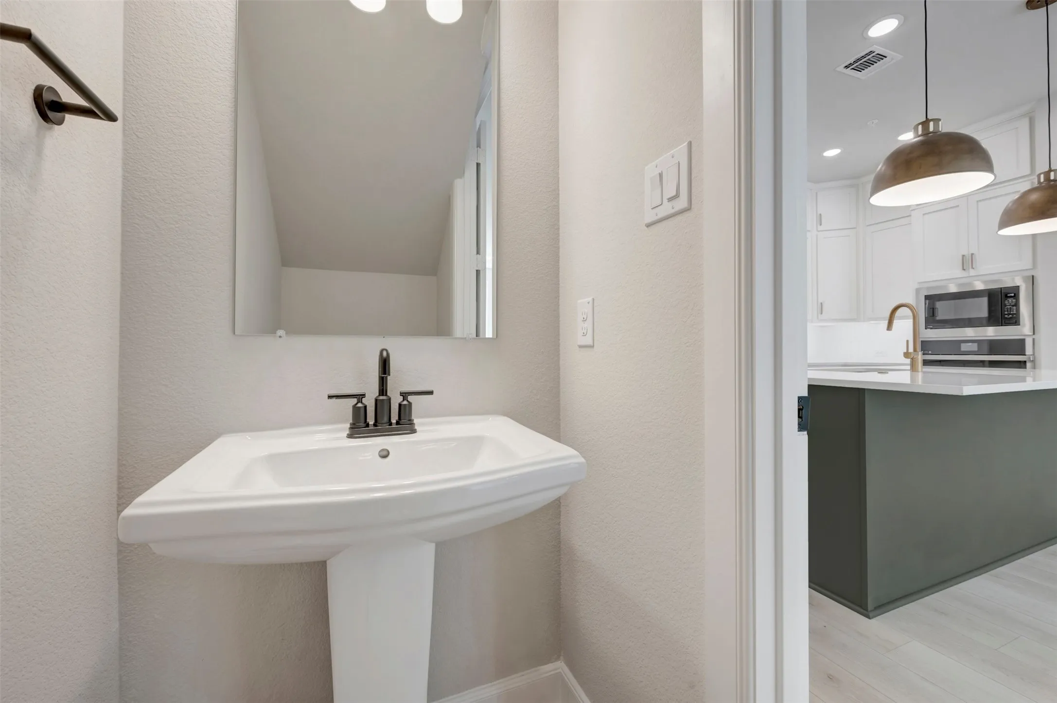Pedestal sink with dark bronze faucet, wall-mounted mirror, and wood-finish flooring