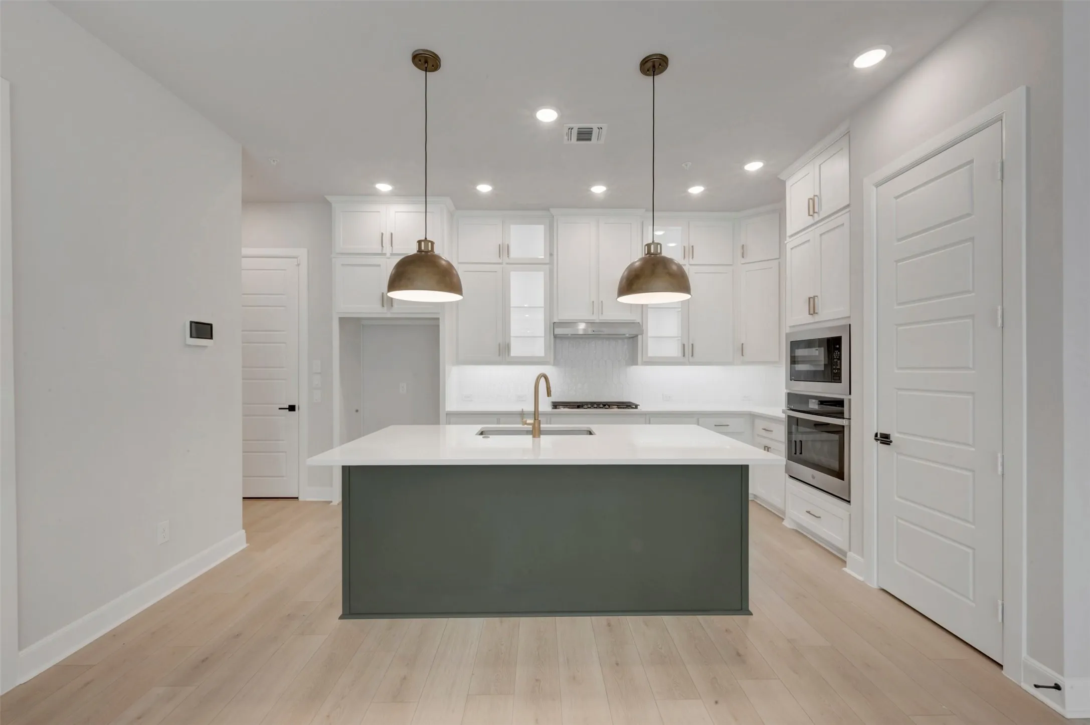 Kitchen featuring a central island with countertop, pendant lighting, built-in stainless steel appliances, white cabinetry, and wood-finish flooring