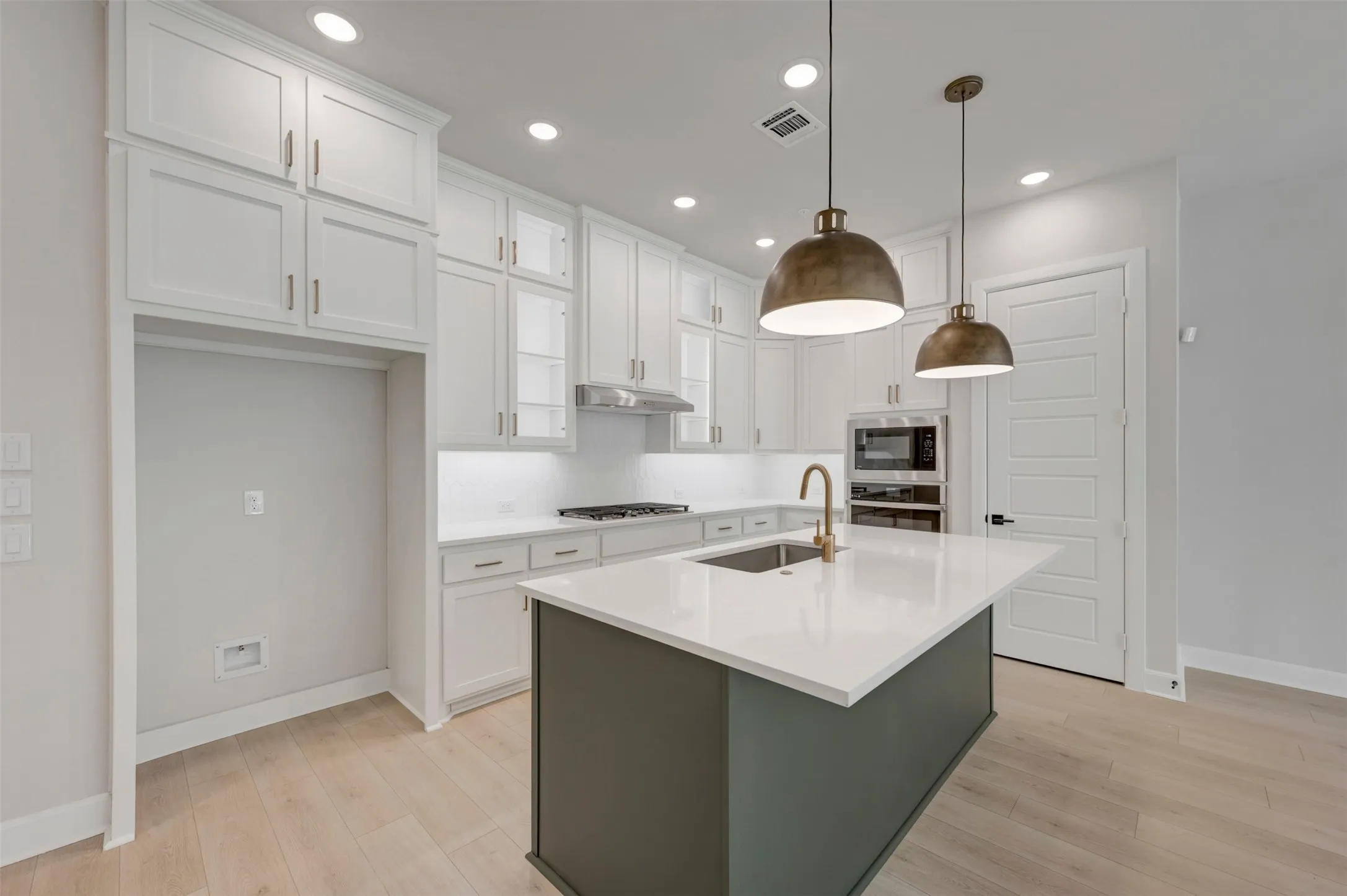 Kitchen featuring white cabinetry, light wood-finish flooring, a central island with a sink and brass-finish faucet, recessed lighting, and pendant lights