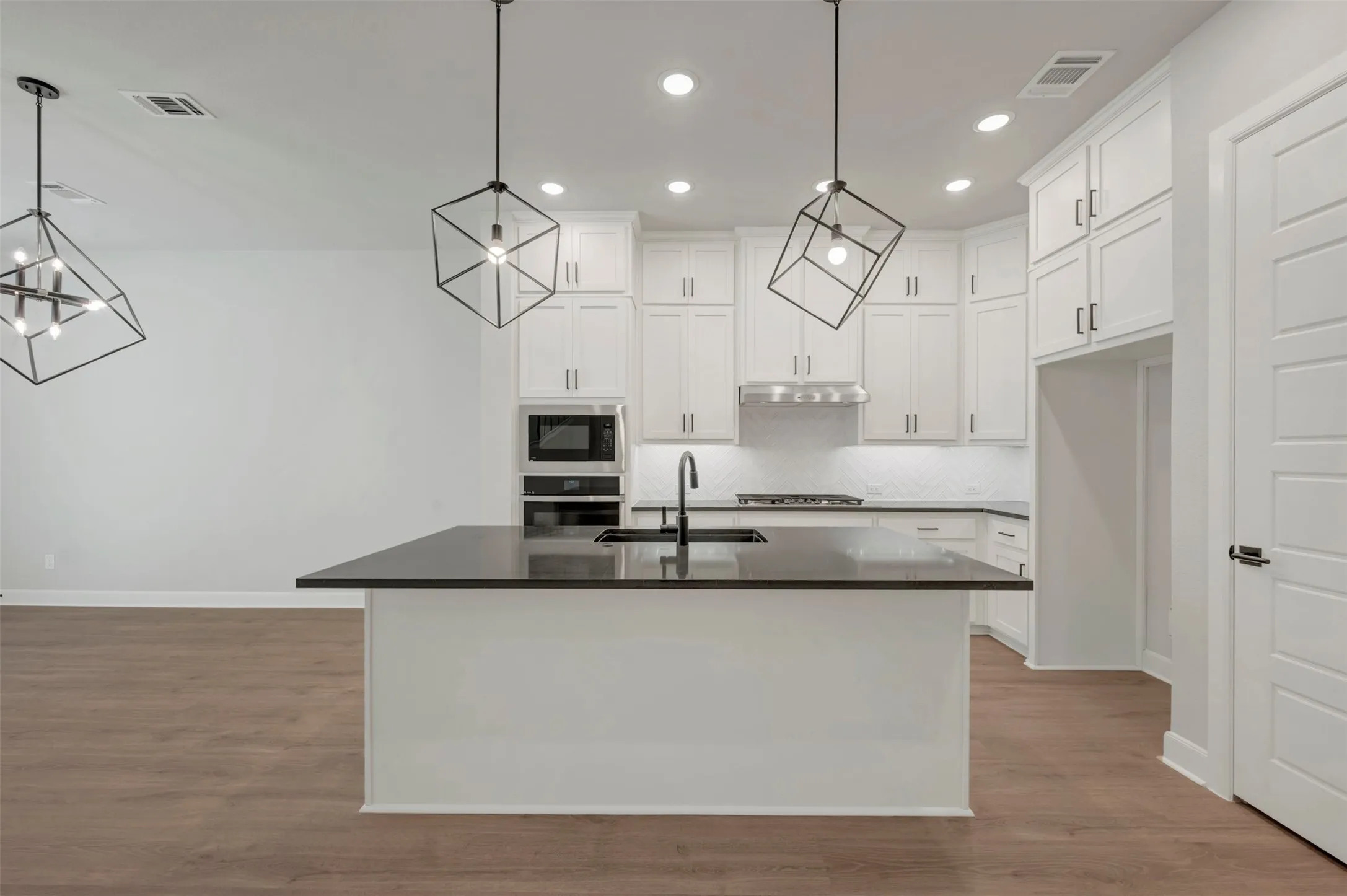 Kitchen featuring a central island with a dark countertop, white cabinetry with dark hardware, built-in stainless steel appliances, and wood-finish flooring