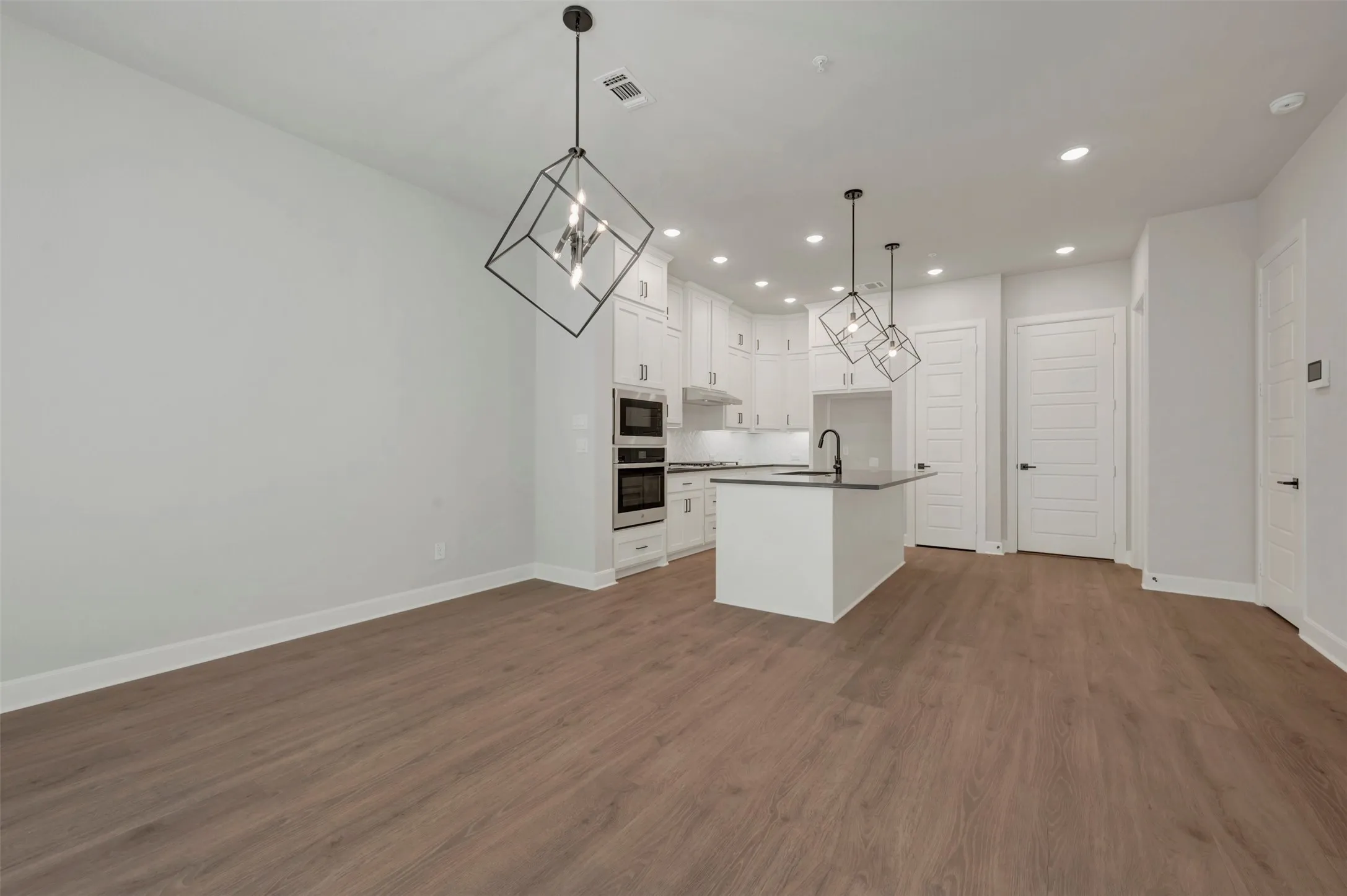 Wood-finish flooring, recessed lighting, white cabinetry, dark countertop island, and stainless steel appliances