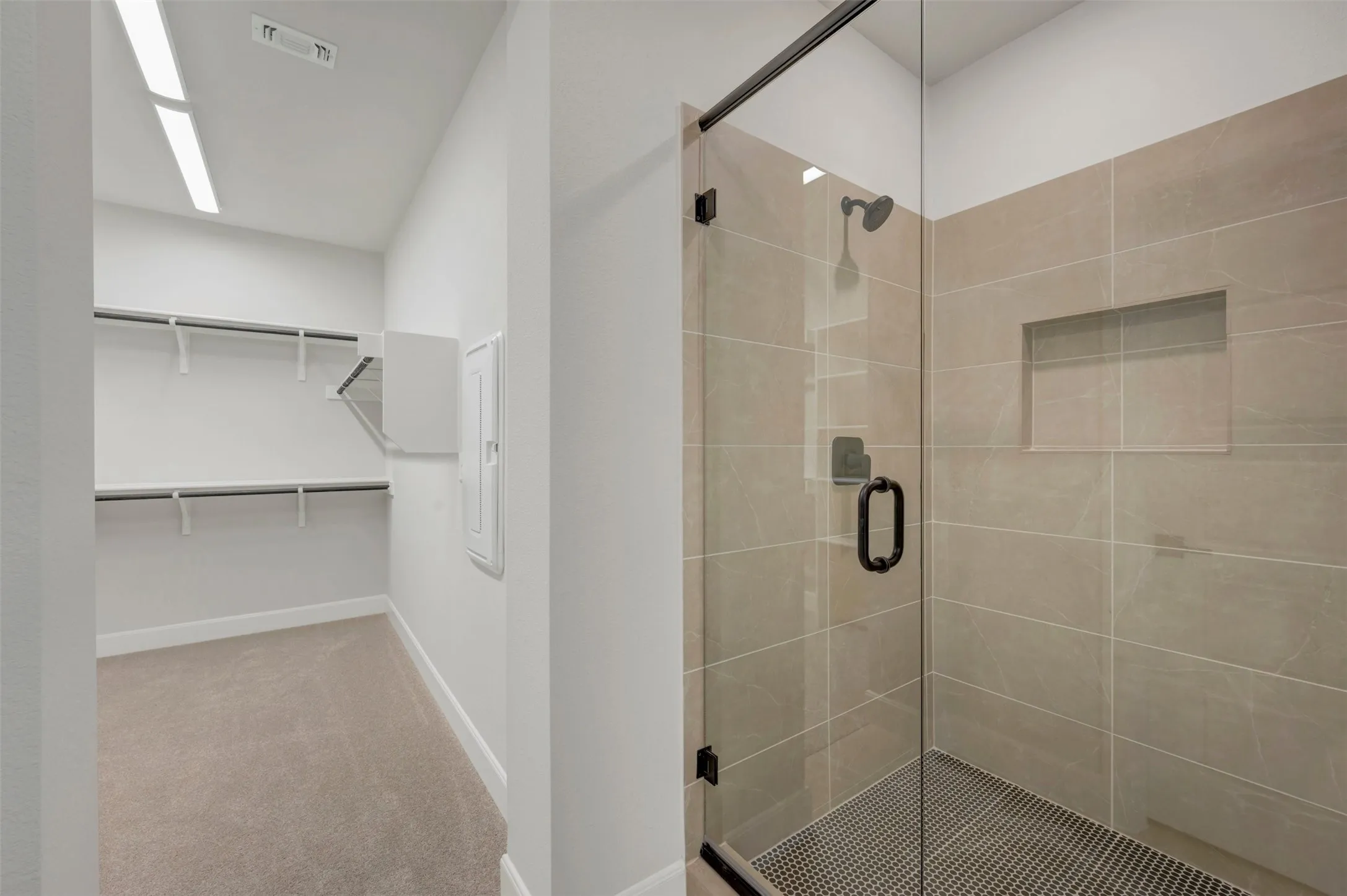 Walk-in closet with built-in shelving, glass-enclosed shower, tiled walls, and a recessed shower niche