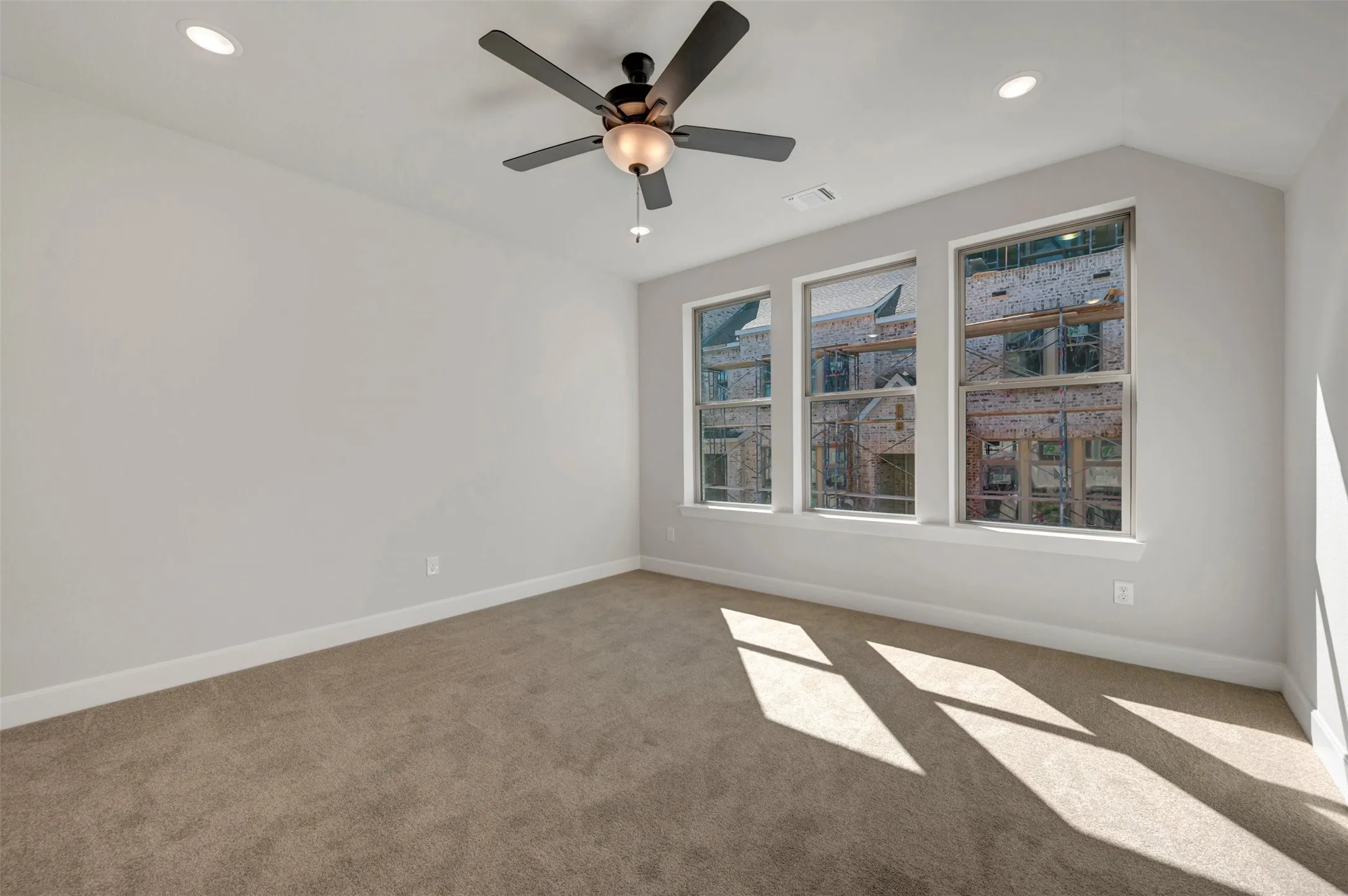 Carpeted flooring, vaulted ceiling, three large windows, ceiling fan, and recessed lighting