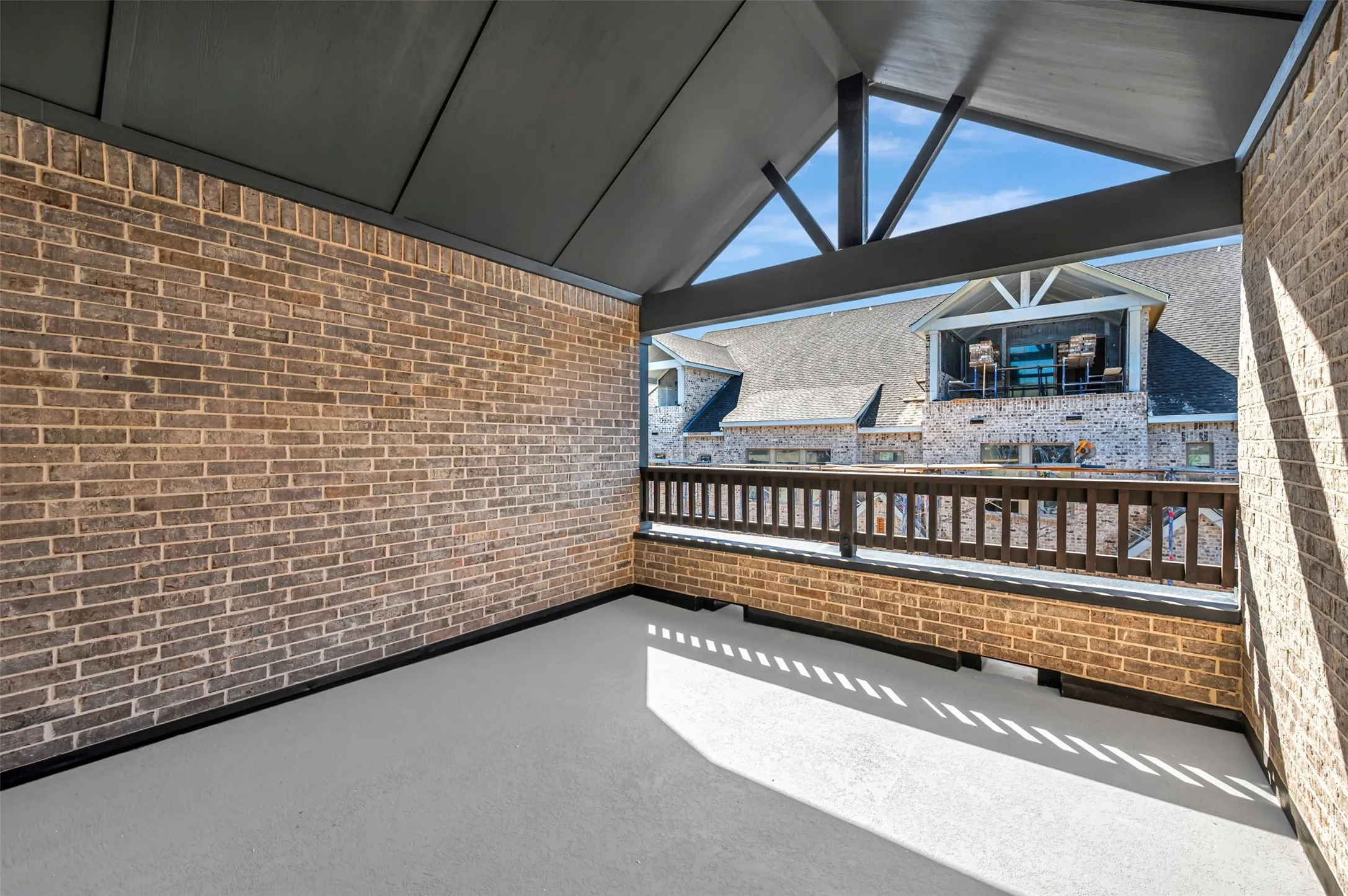 Covered porch with exposed brick walls, a sloped ceiling, and a dark wood-finish railing