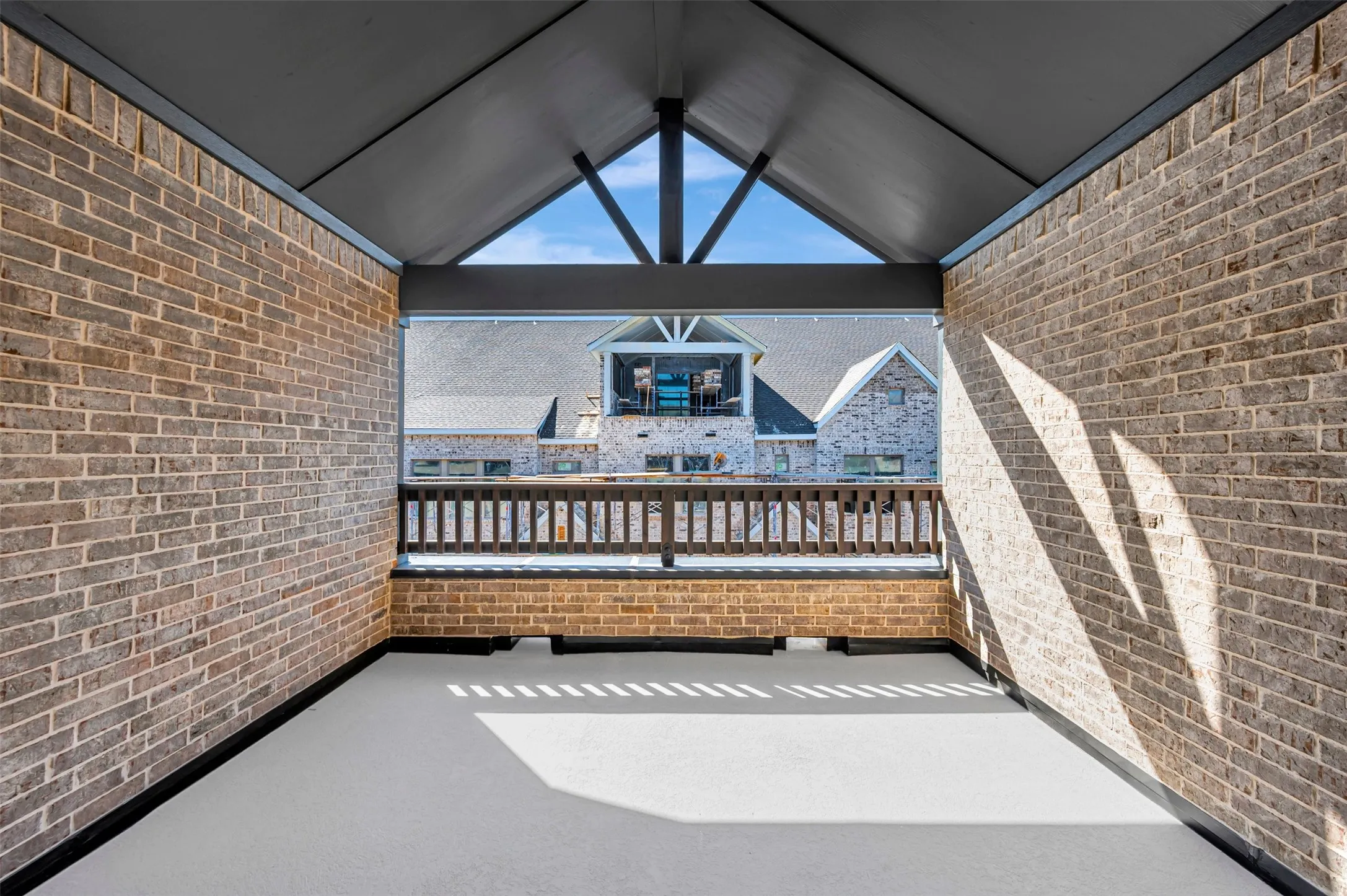 Covered outdoor space featuring brick walls, an open gable roofline, and a wood railing
