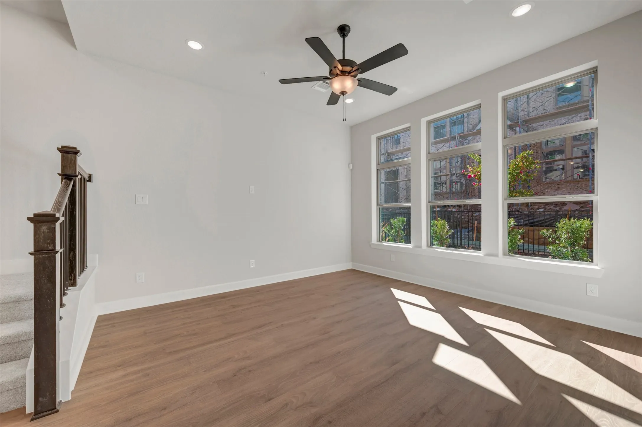 Recessed lighting, ceiling fan with integrated lighting, wood-finish flooring, white walls, and a staircase with dark wood newel posts and railings