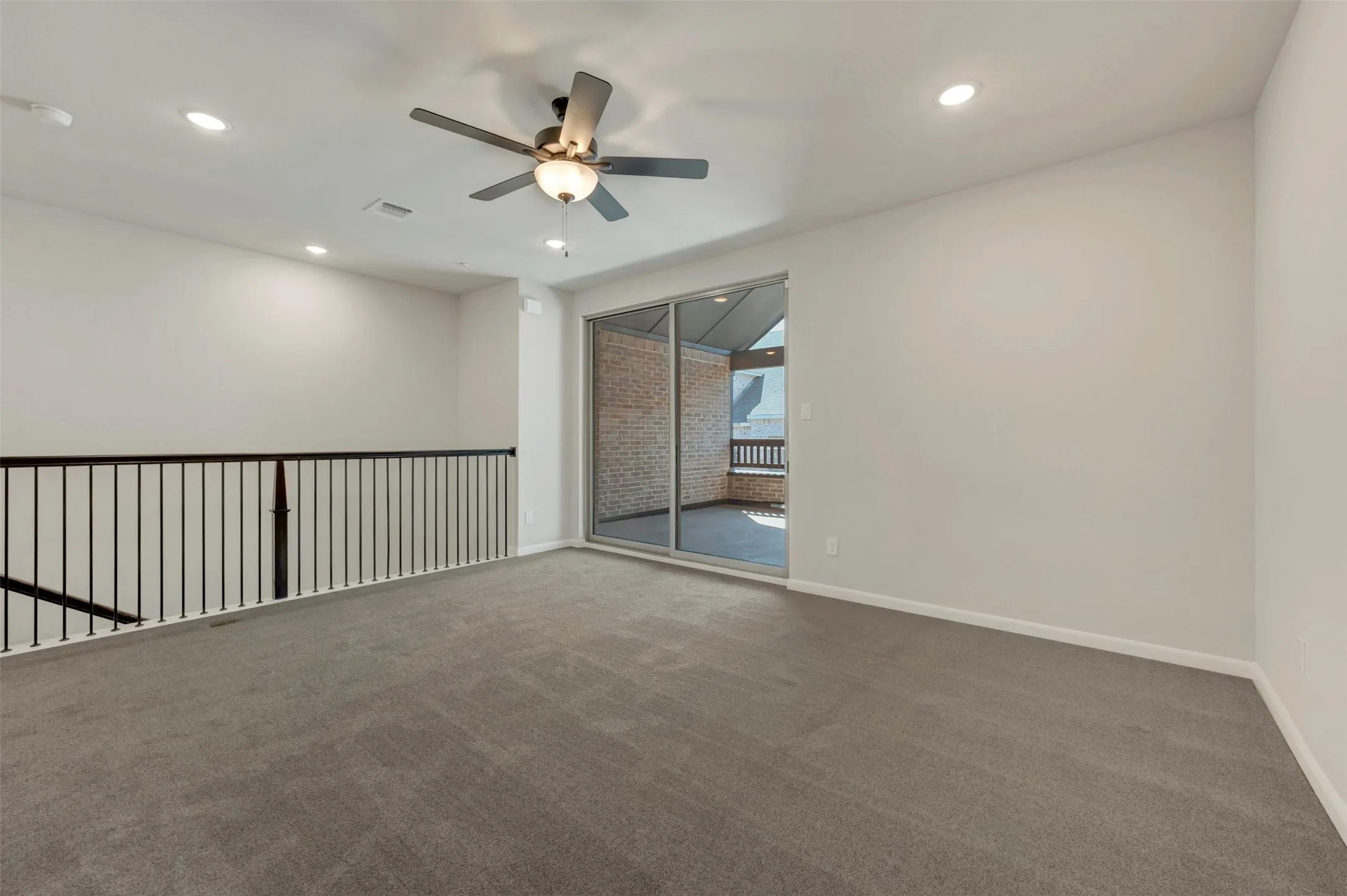 Spacious carpeted room featuring a ceiling fan with integrated lighting, recessed ceiling lights, and a sliding glass door leading to an outdoor space with a brick wall