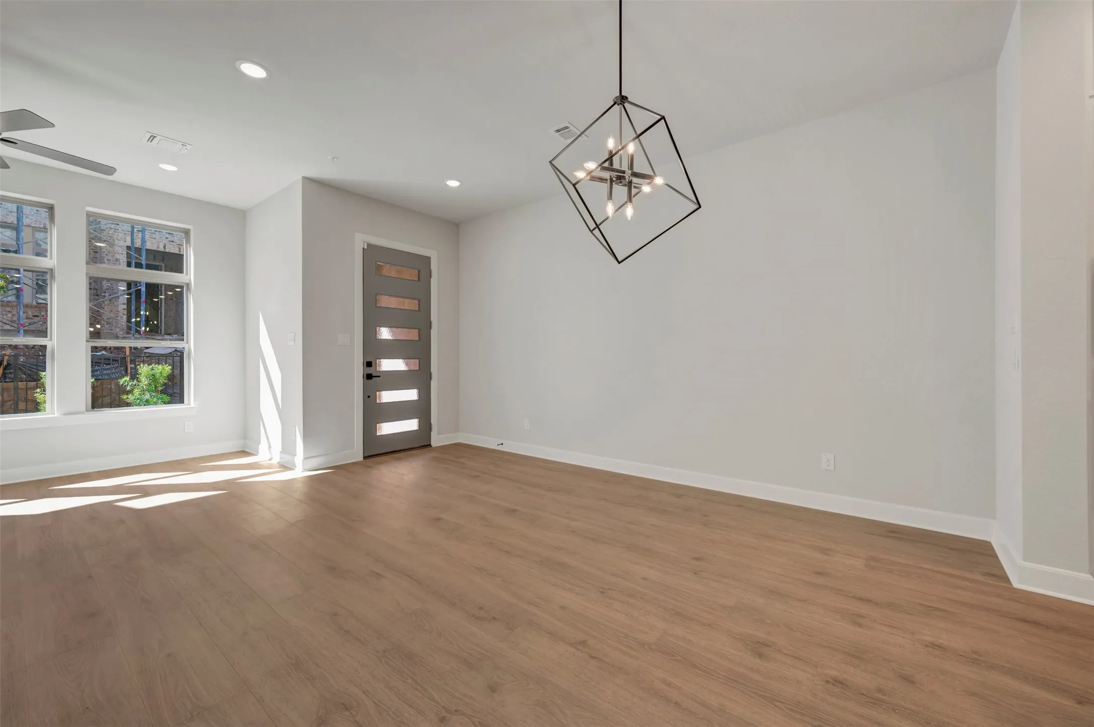 Spacious room featuring wood-finish flooring, multiple windows, a modern geometric chandelier, and recessed lighting