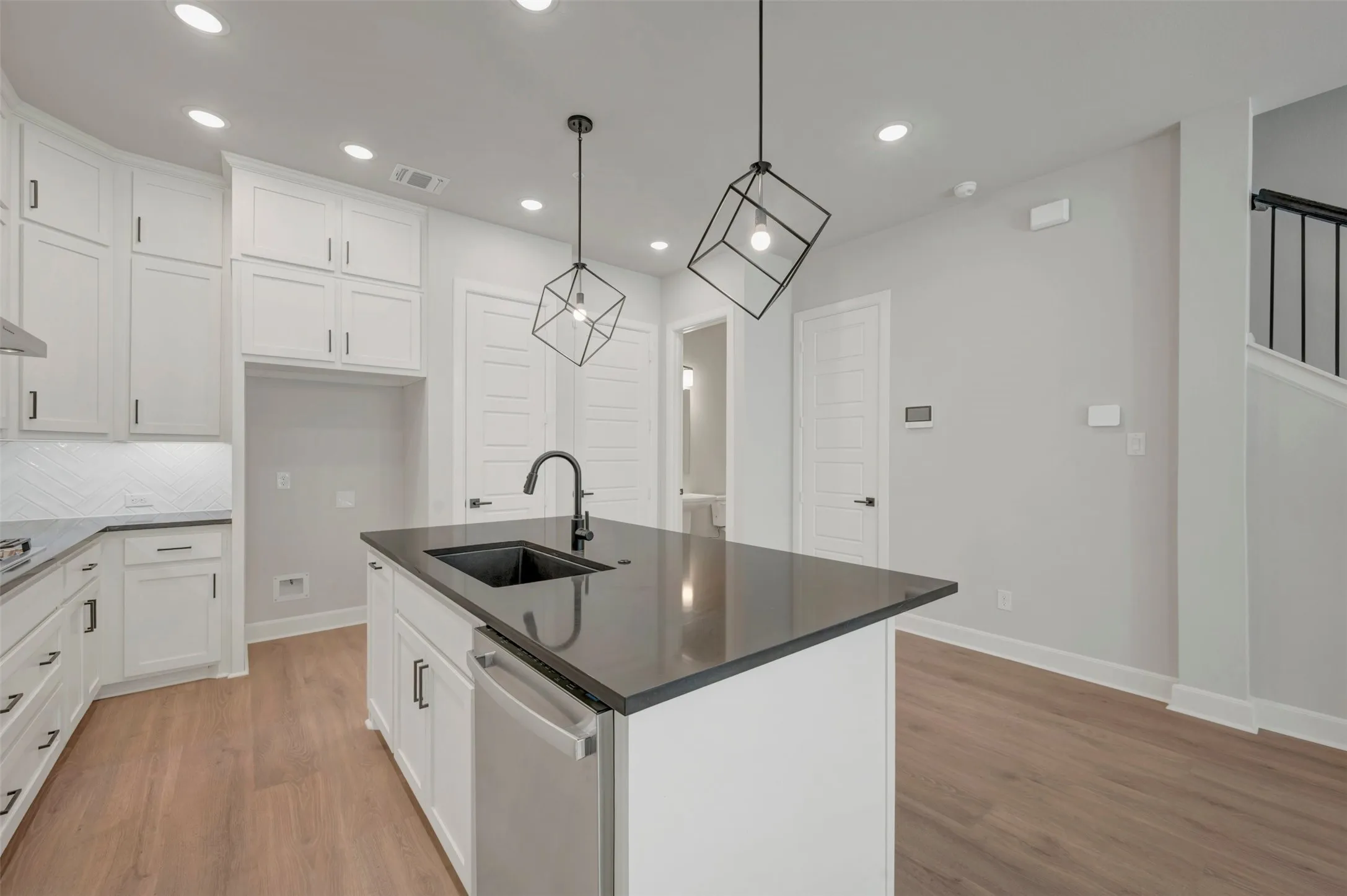 Kitchen featuring white cabinetry, dark countertops, wood-finish flooring, recessed lighting, and a kitchen island with an integrated sink and modern pendant lighting