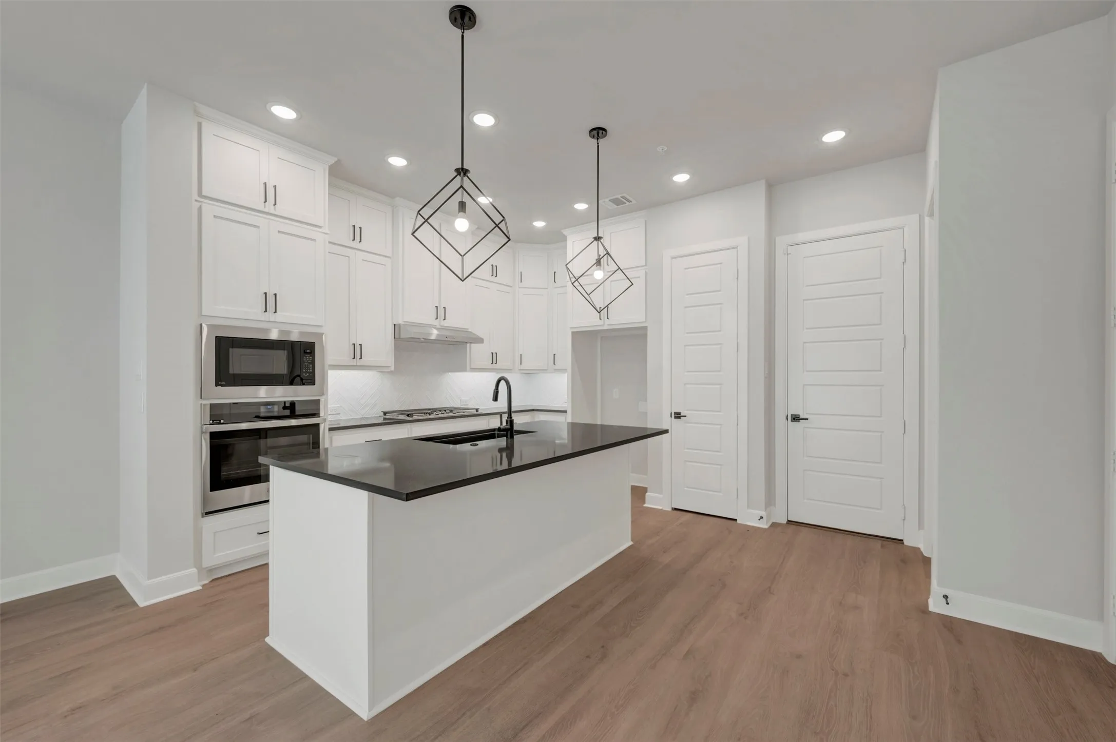 Kitchen featuring white cabinetry, a dark countertop island with an integrated sink, stainless steel appliances, and wood-finish flooring