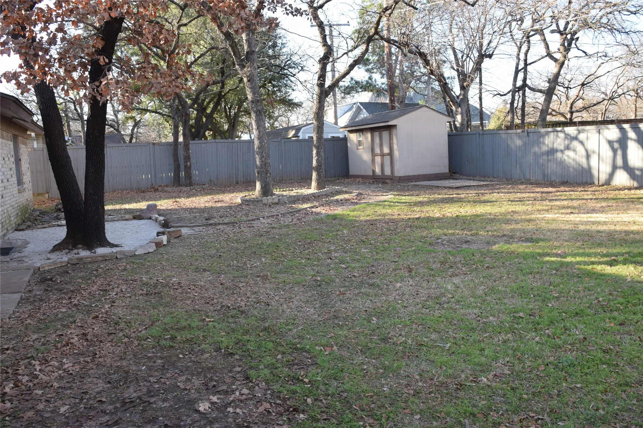 Spacious fenced backyard featuring a storage shed, mature trees, and a gravel patio area
