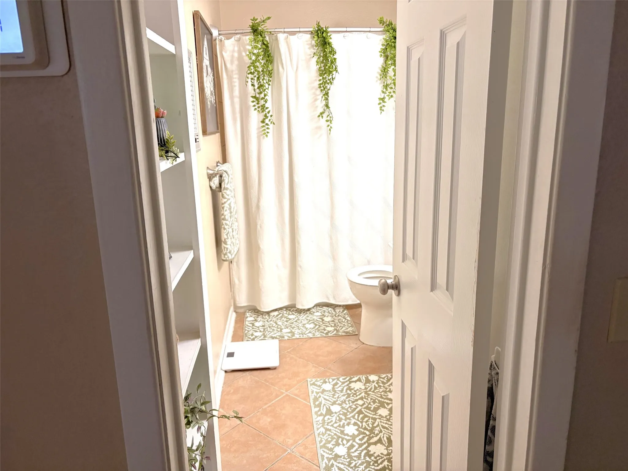 Bathroom featuring terracotta-toned flooring, a shower/tub combination with a white curtain, and a built-in shelving unit