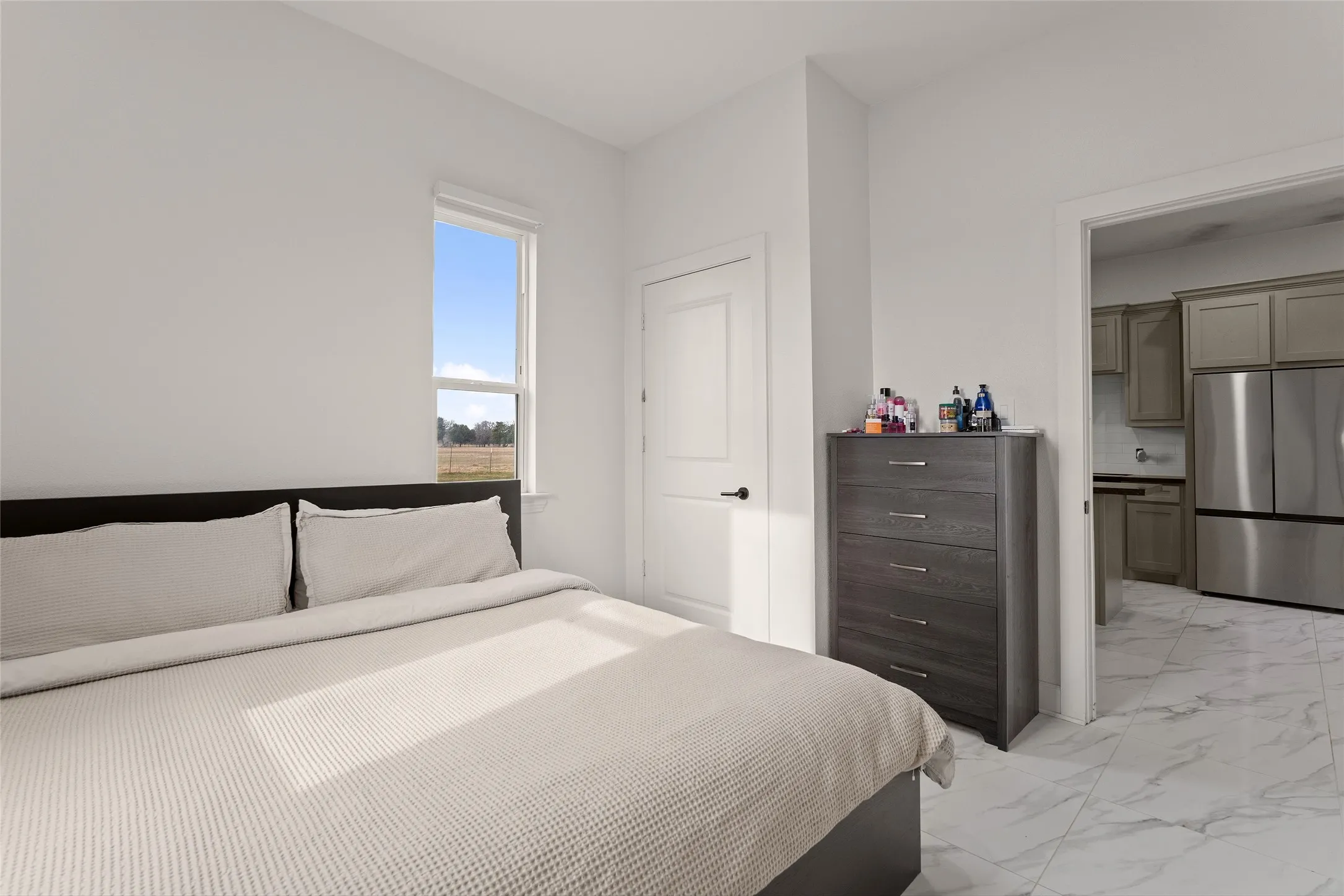 Bright room featuring a window overlooking an open field, white walls, and white marble-look tile flooring