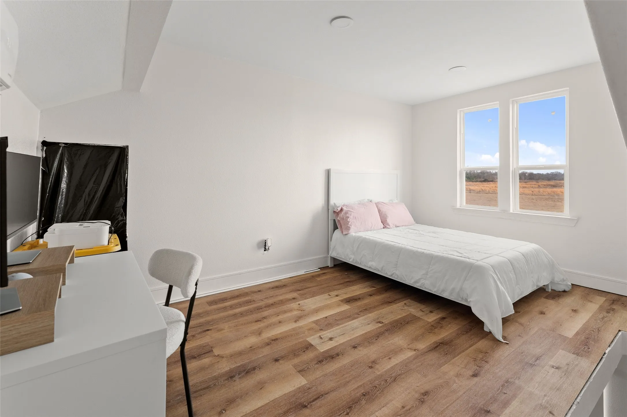 Bright room featuring dual windows with white trim, wood-finish flooring, a white headboard, and a white baseboard