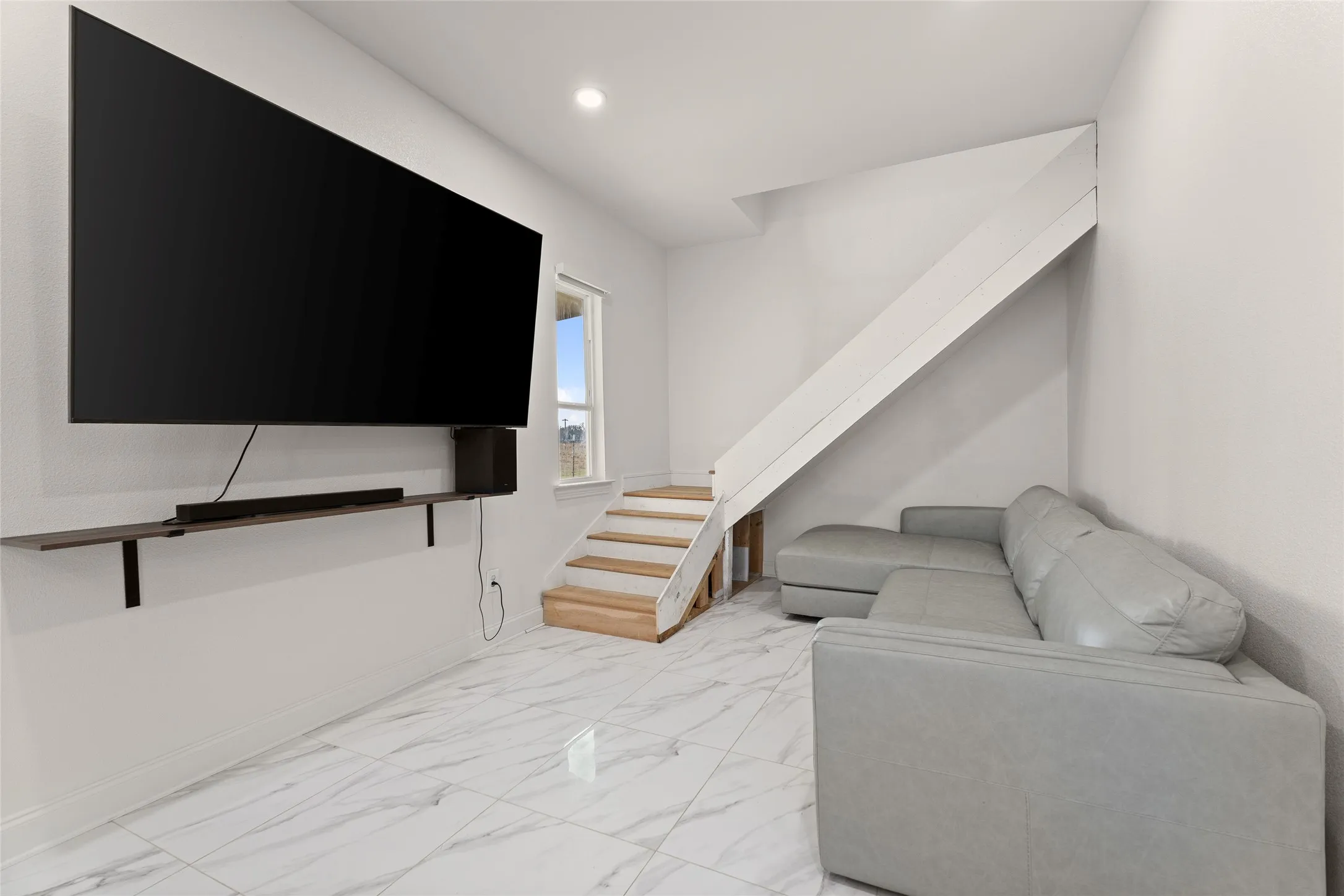 Living area featuring large format tile flooring, a wall-mounted entertainment shelf, natural wood stair treads, and a window providing natural light