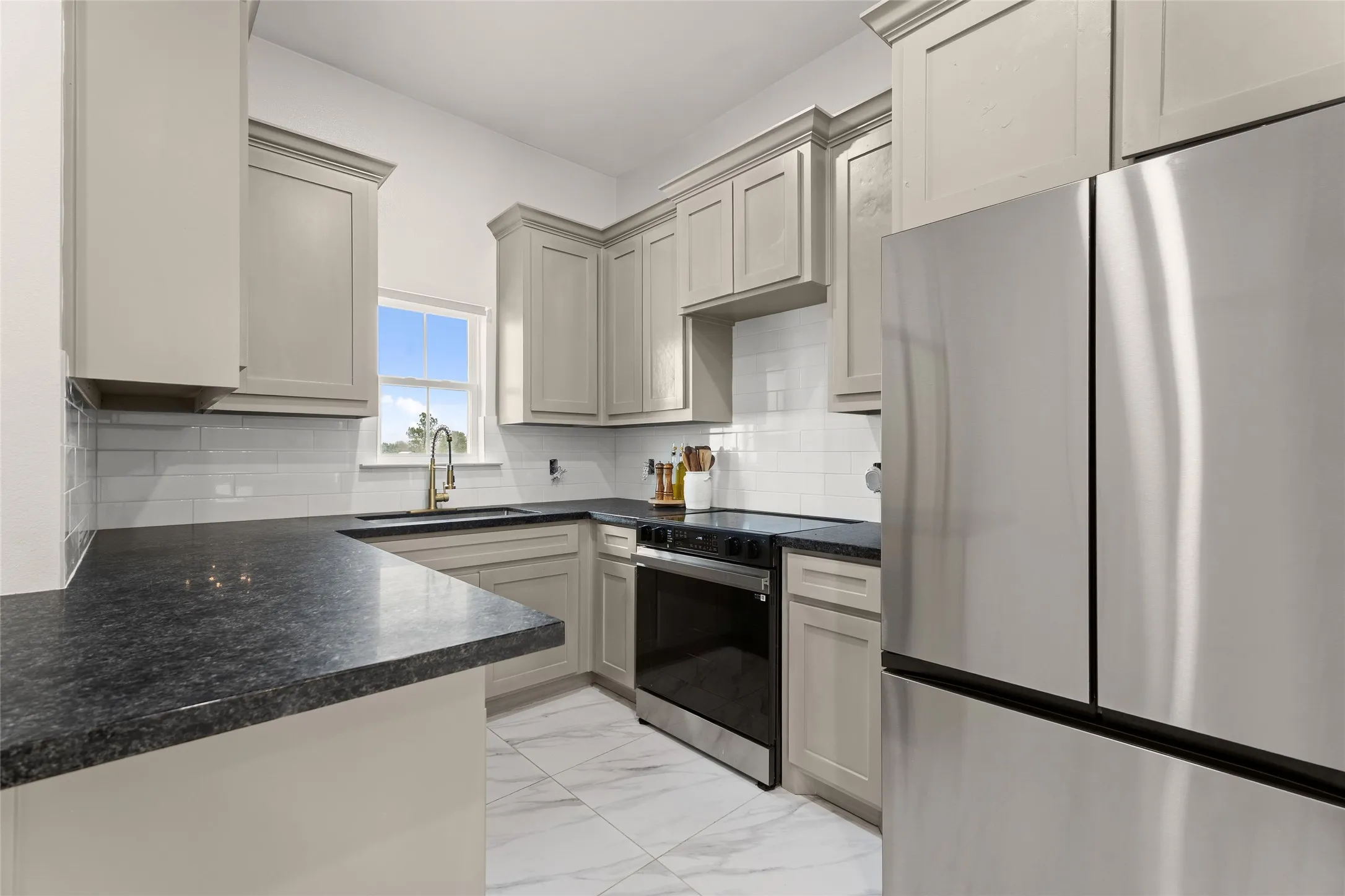 Kitchen featuring light cabinetry, dark countertops, white subway tile backsplash, and a stainless steel appliance suite