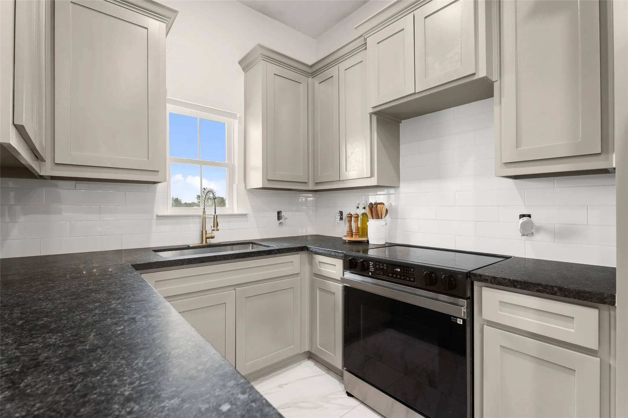 Kitchen featuring light-toned cabinetry, dark countertops, a stainless steel range, and a brass-finished faucet