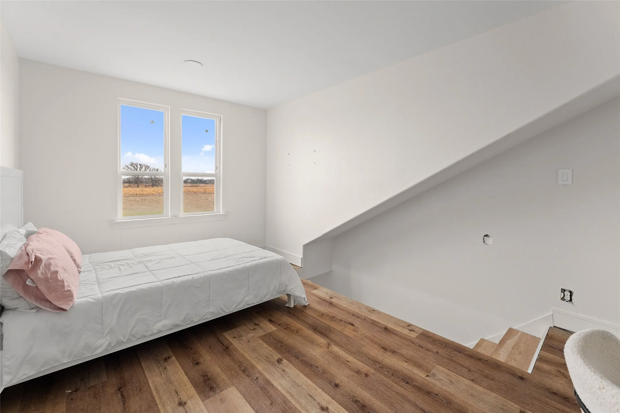 Spacious room featuring wood-finish flooring, white walls, and a pair of windows providing natural light