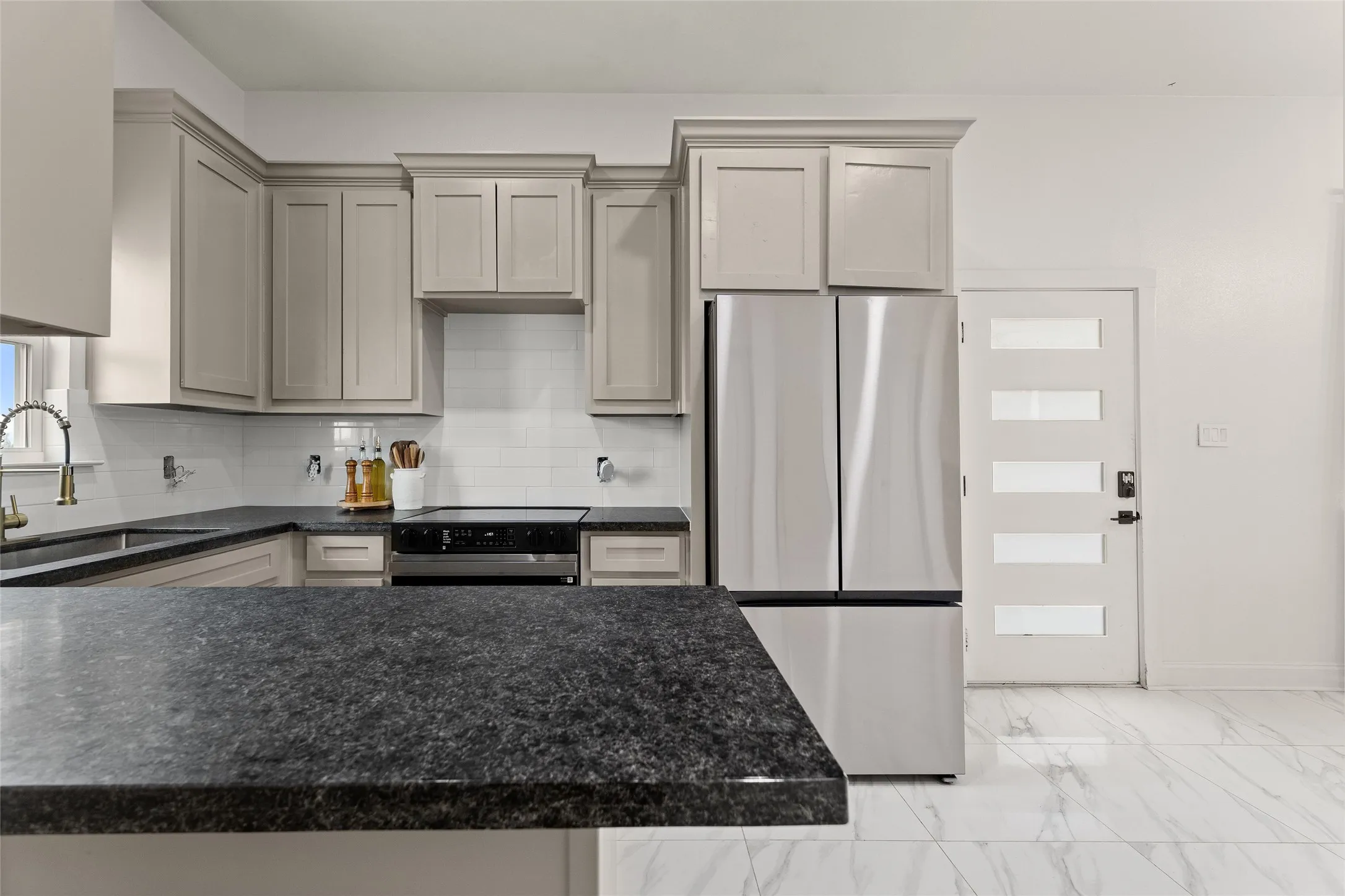 Contemporary kitchen featuring dark countertops, light gray cabinetry, stainless steel appliances, and a white subway tile backsplash