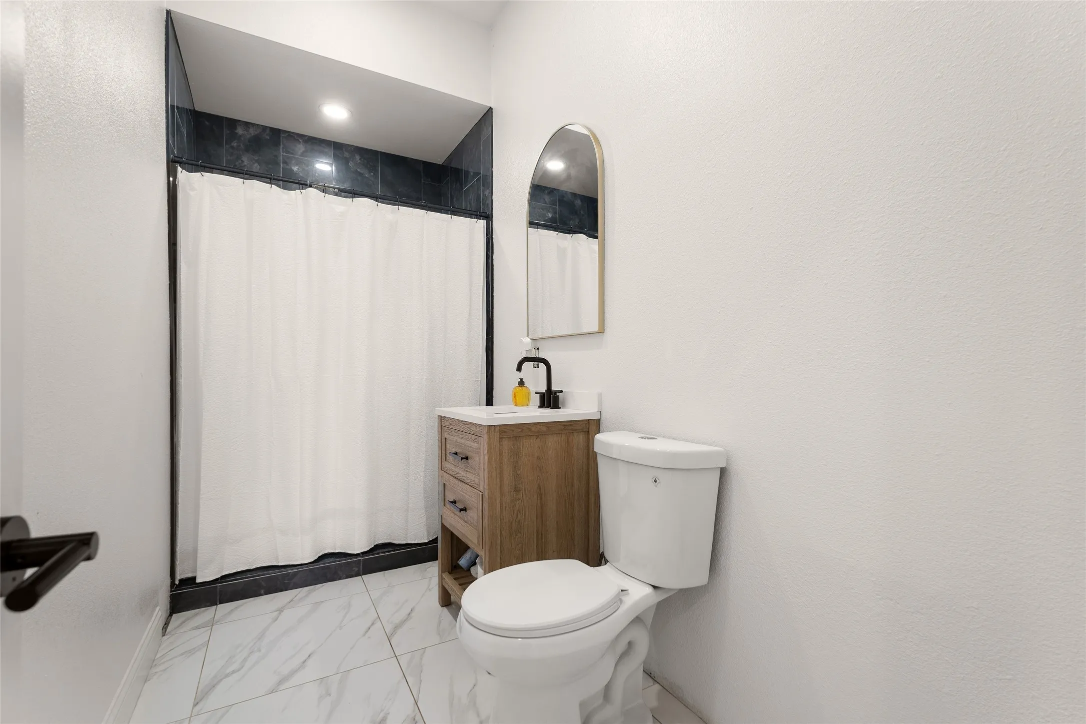 Bathroom featuring a shower with dark tiled surround, white shower curtain, and recessed lighting