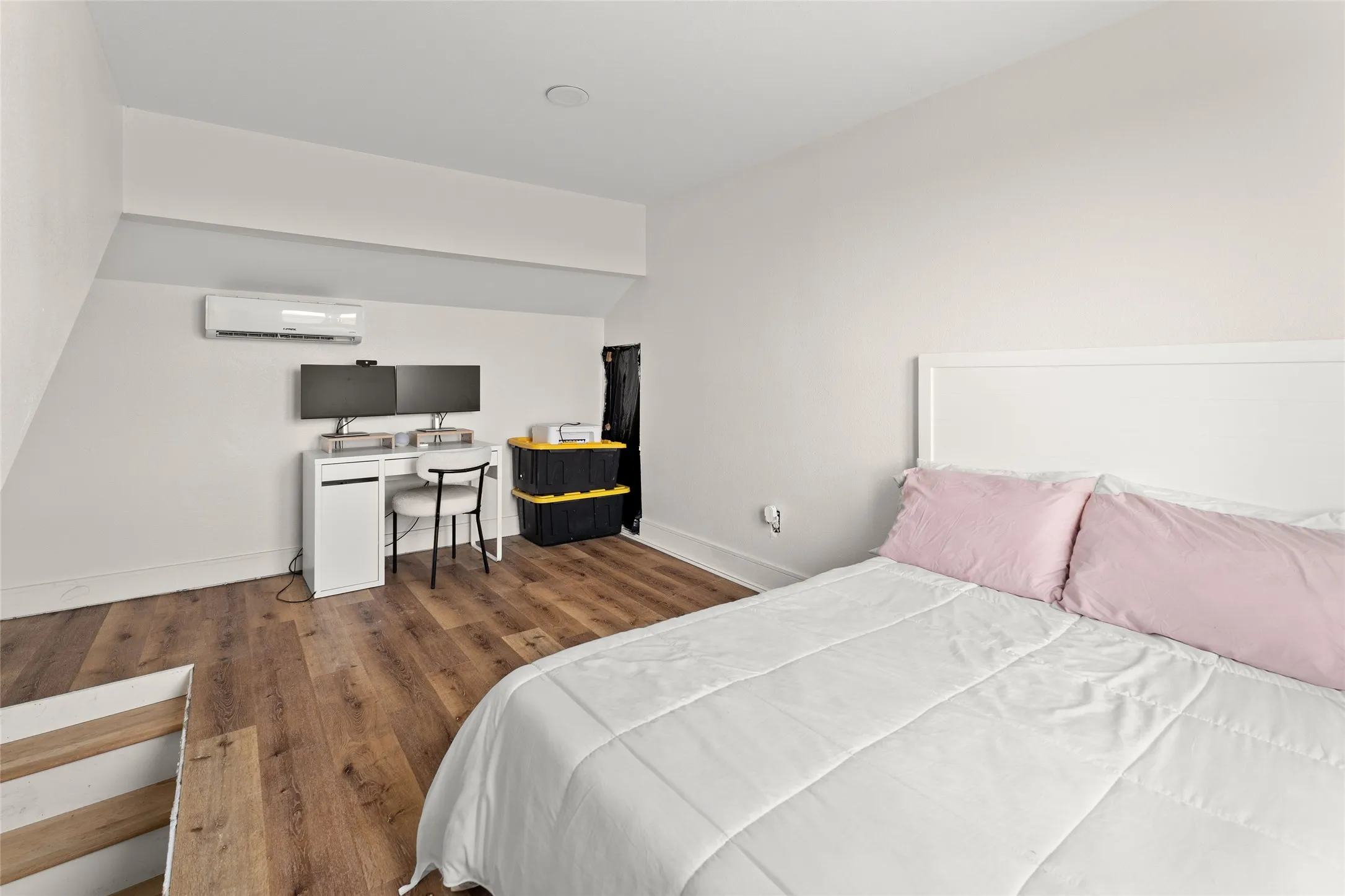 Room featuring wood-finish flooring, a white headboard, a wall-mounted ductless mini-split system, and a recessed ceiling light