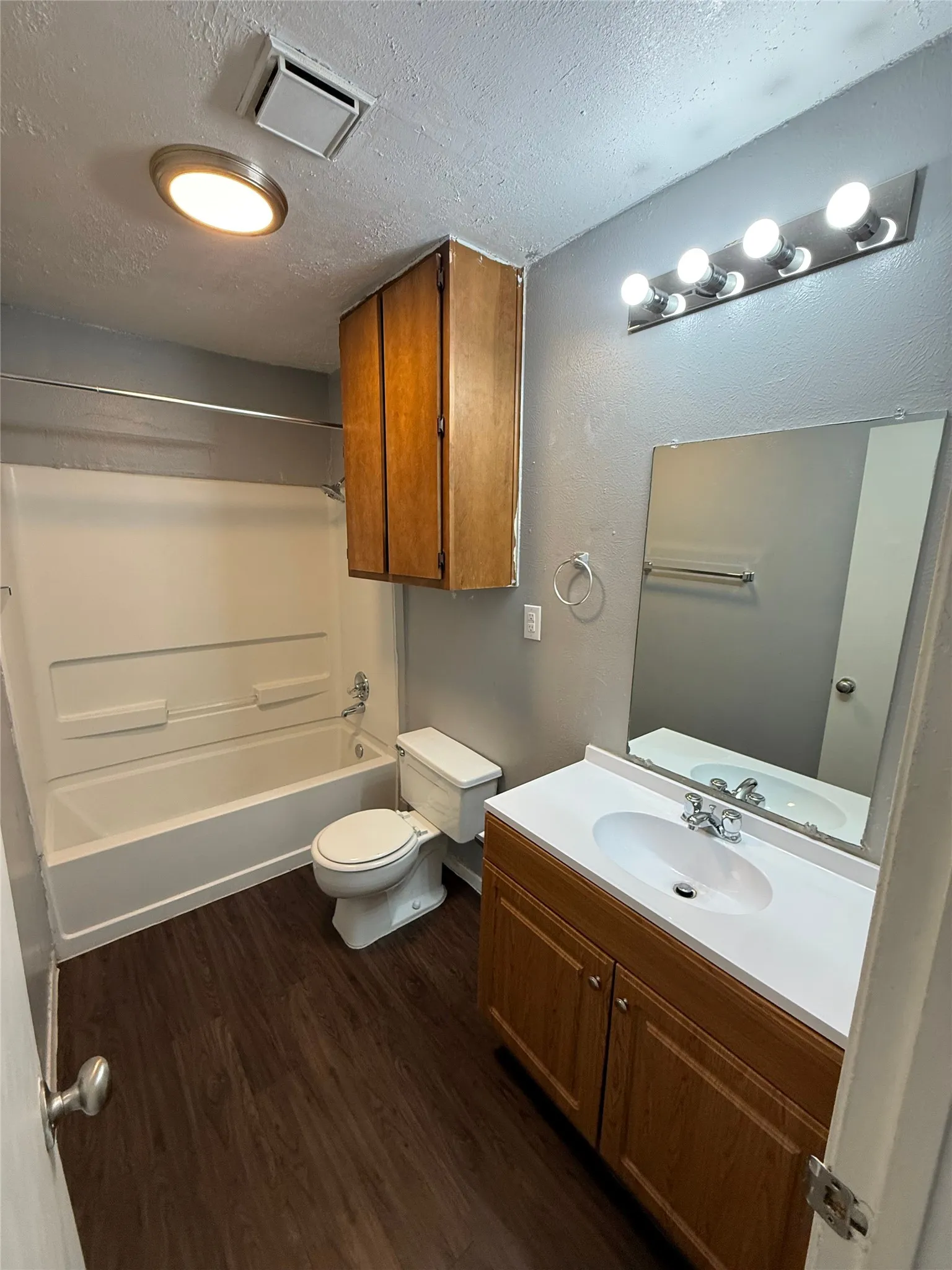 Full bathroom featuring wood-finish flooring, a white tub and shower combination, a single vanity with a white countertop and integrated sink, and a mirrored wall