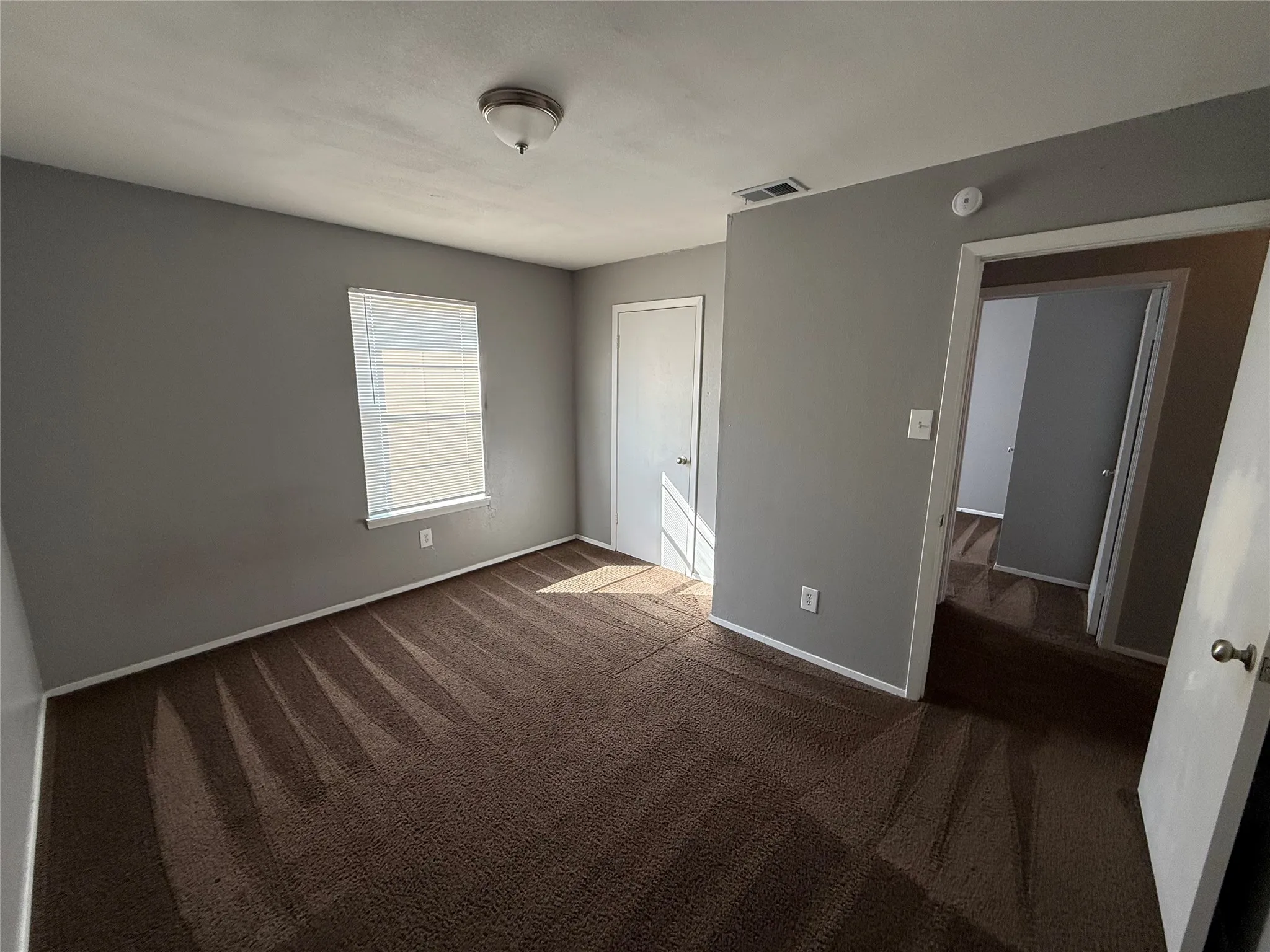Carpeted room featuring neutral gray walls, white trim, a single window, and a flush-mount ceiling light fixture