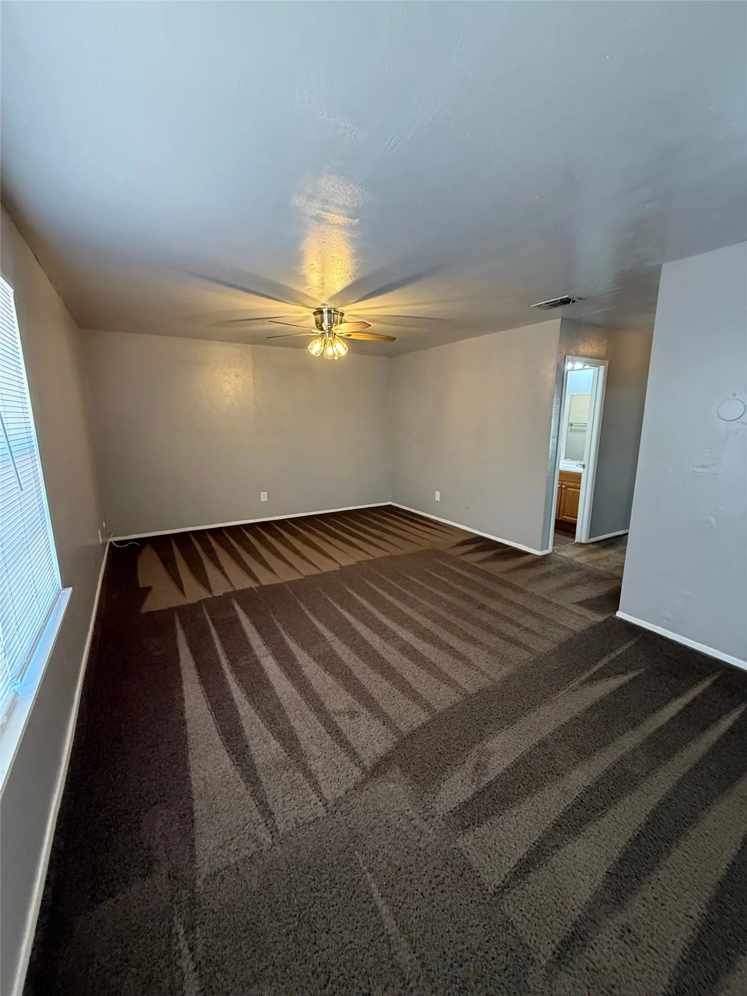 Spacious room featuring broadloom carpeting, a ceiling fan with integrated lighting, and a window with horizontal blinds