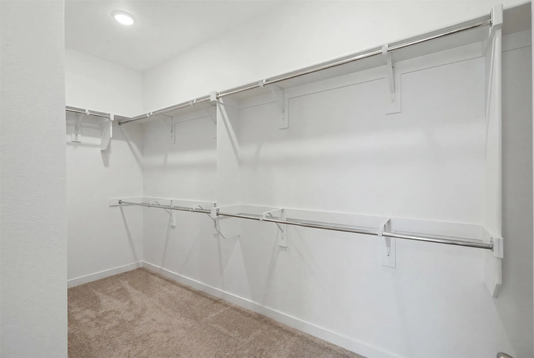 Spacious primary walk-in closet featuring double hanging rods, built-in shelving, plush carpet, and recessed lighting.