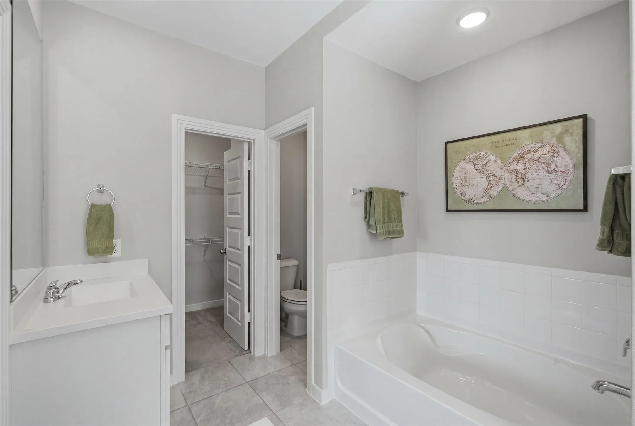 Primary bathroom featuring a soaking tub, white vanity, tile flooring, recessed lighting, and direct access to the walk-in closet.