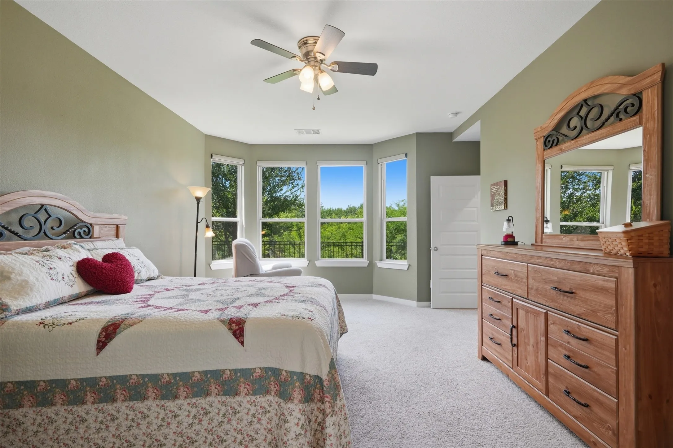 Spacious primary bedroom featuring plush carpet, ceiling fan, a large bay window with greenbelt views, and a private walk-in closet.