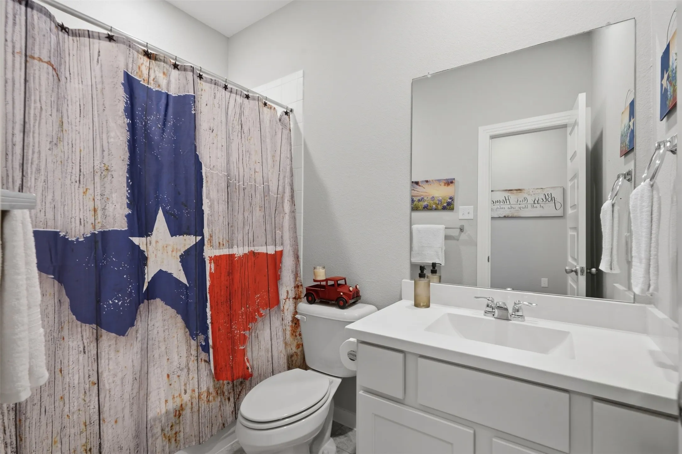 Clean and functional bathroom with a white single sink vanity, large mirror, shower-tub combo, and neutral tones throughout.