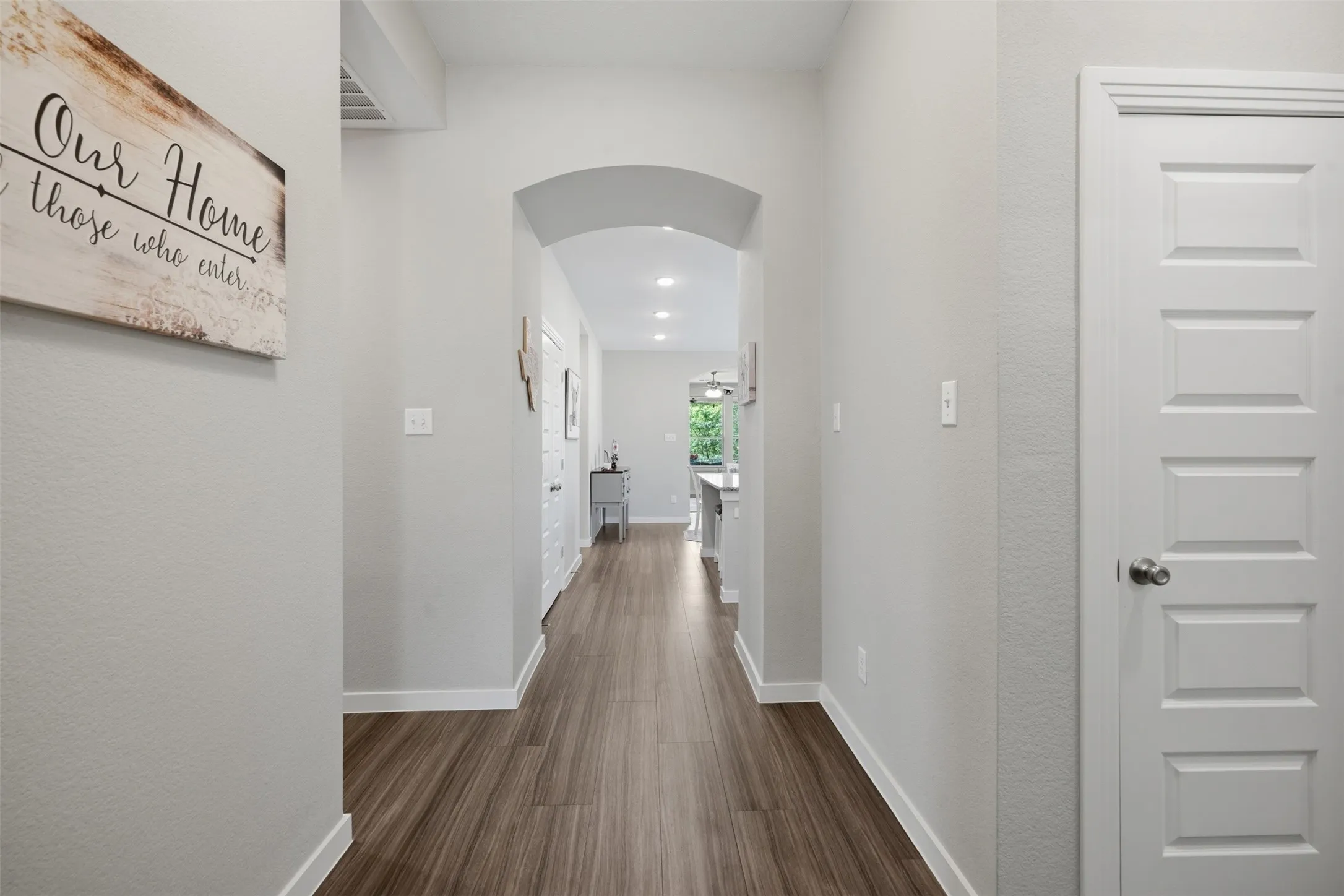 Welcoming entryway featuring wood look flooring, an elegant arched hallway, and a bright open view to the main living area.