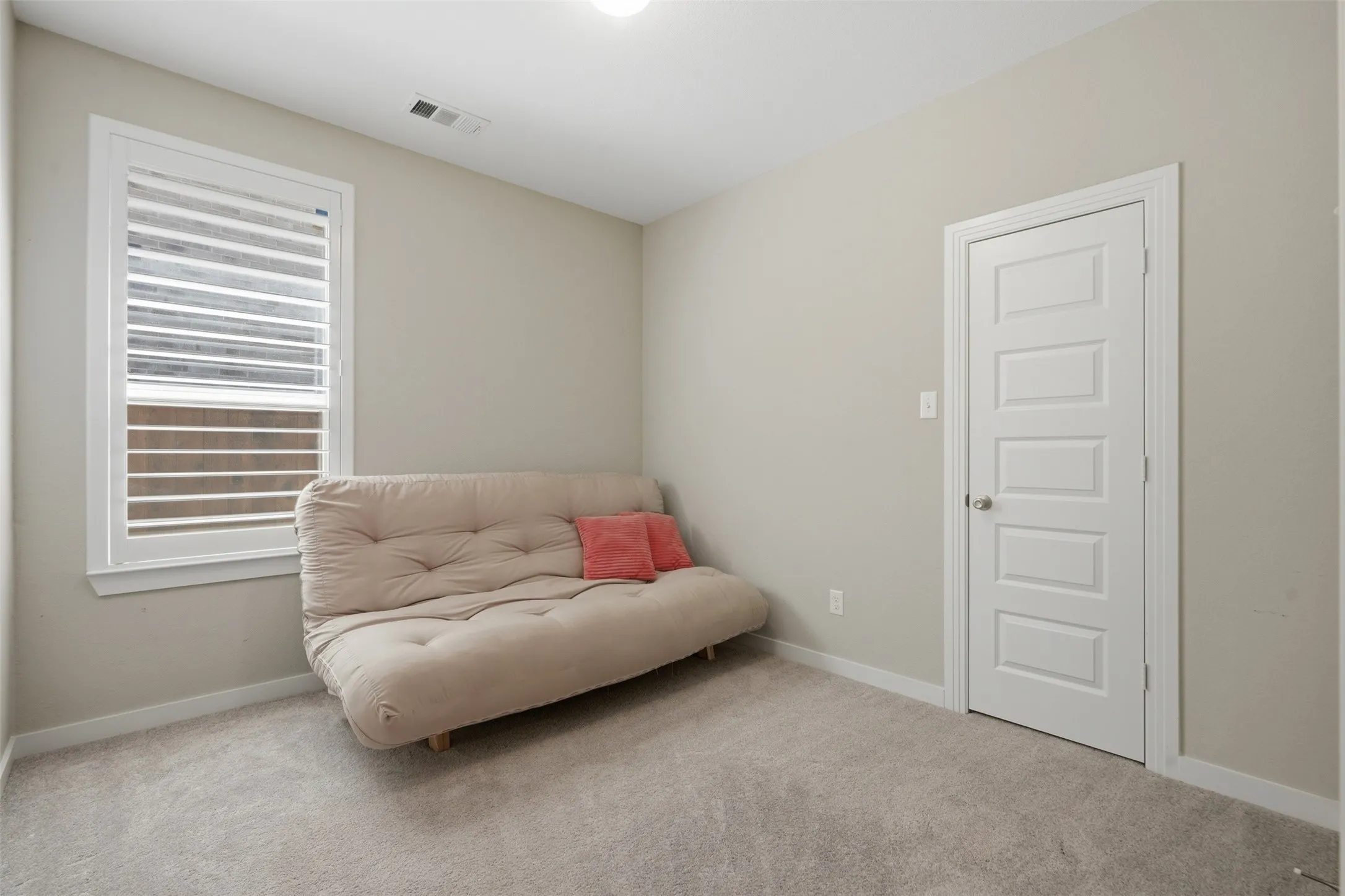 Bedroom featuring plush carpet flooring, neutral paint, plantation shutter window, and a simple clean layout ready for any use.