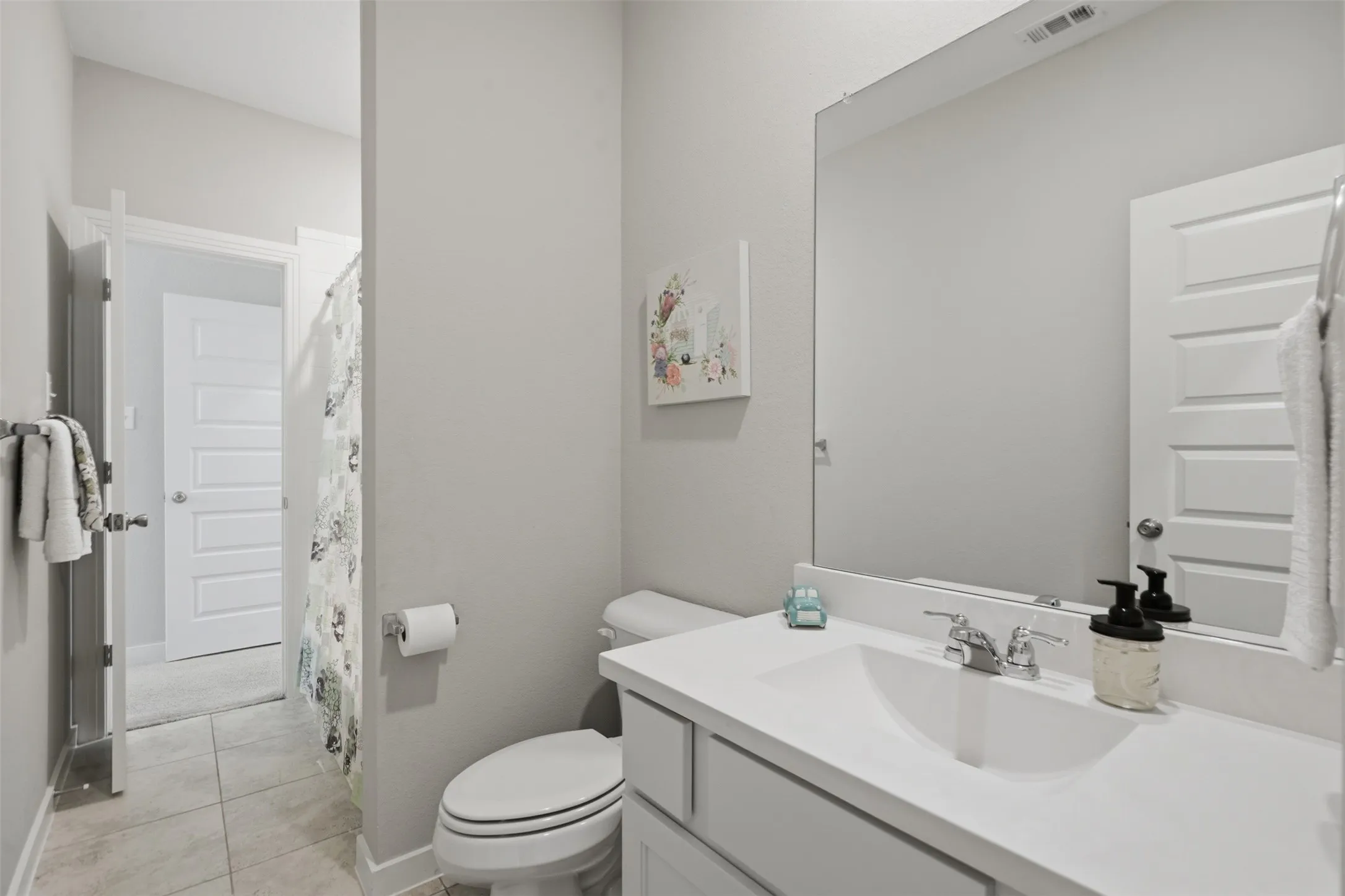 Bright secondary bathroom featuring white cabinetry, single sink vanity, large wall mirror, shower tub combination, and tile flooring.