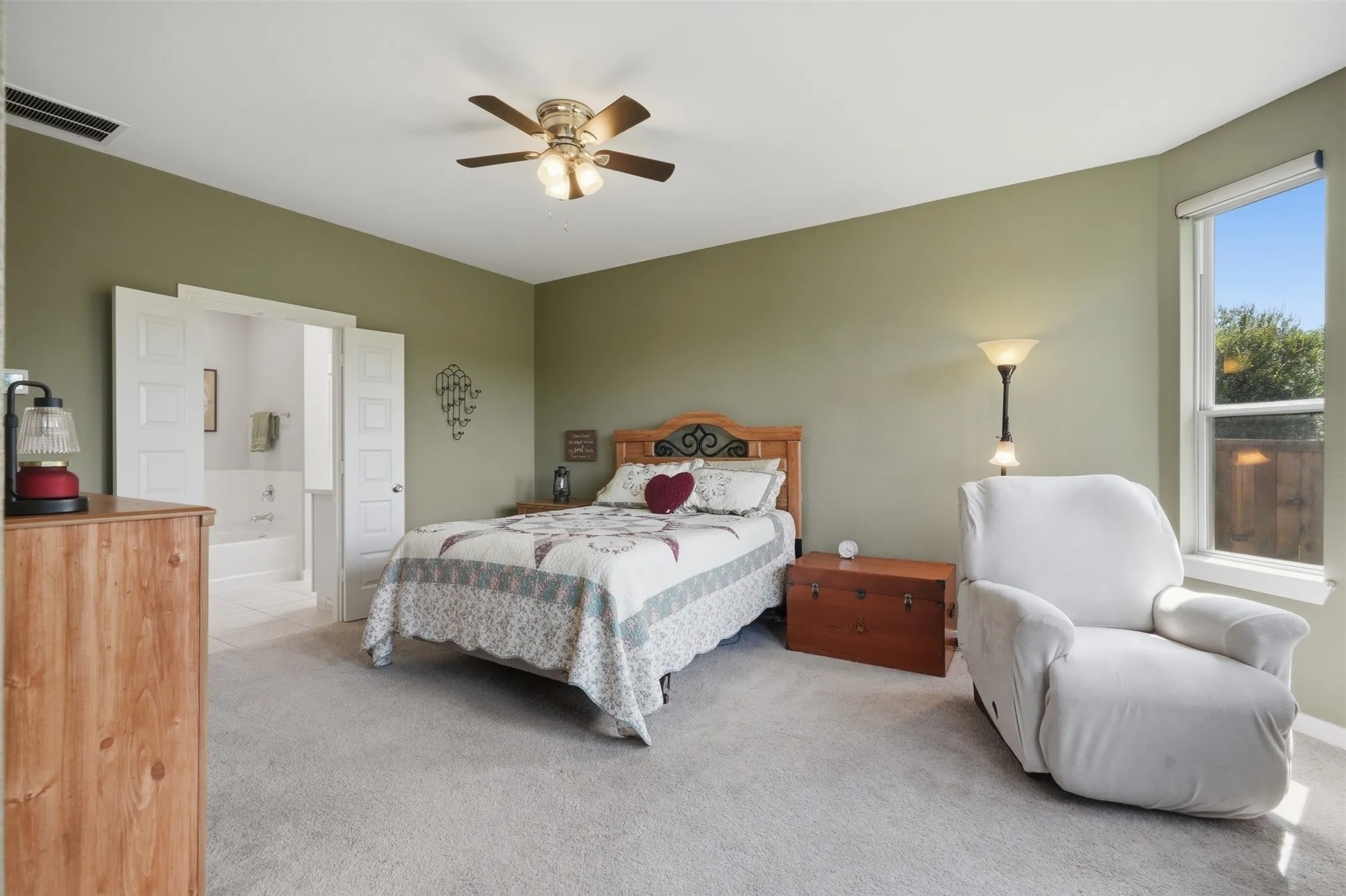 Well-sized primary bedroom boasting plush carpet, ceiling fan, natural light from large windows, and a connected bathroom