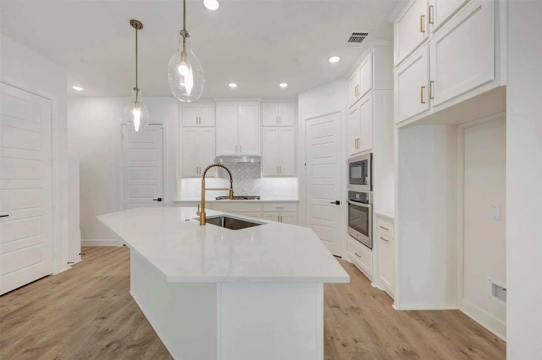 Kitchen featuring a large island with sink, white cabinetry with gold-tone hardware, built-in stainless steel appliances, and wood-finish flooring
