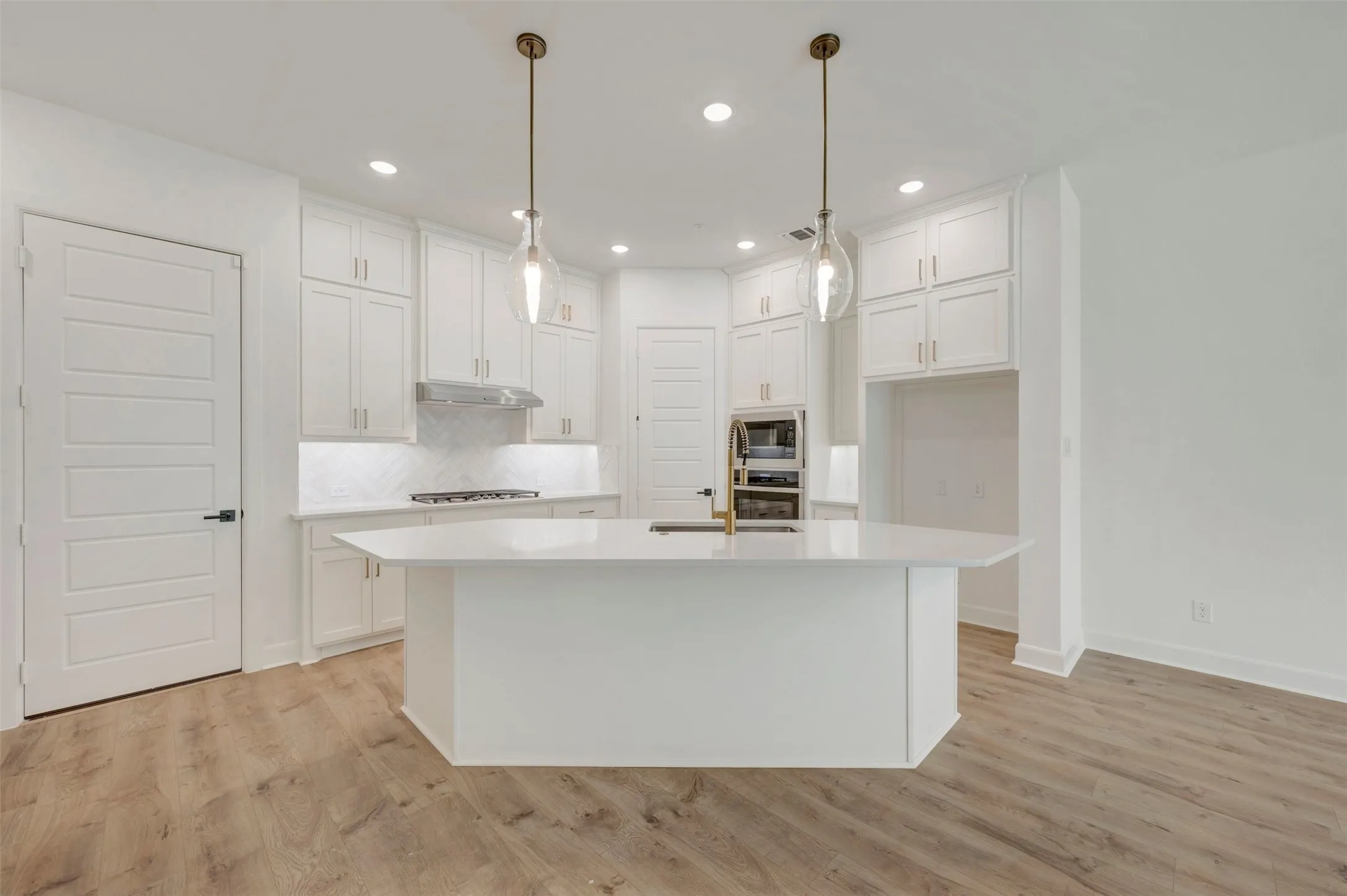 White kitchen featuring wood-finish flooring, white cabinetry, a center island with a sink, and pendant lighting
