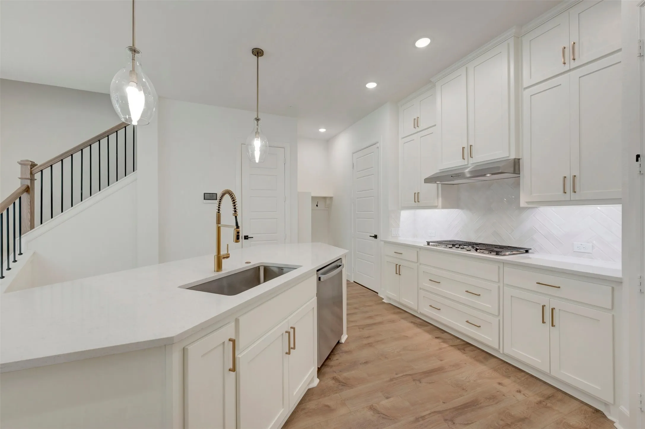 White cabinetry, stainless steel appliances, wood-finish flooring, island with undermount sink, and recessed lighting