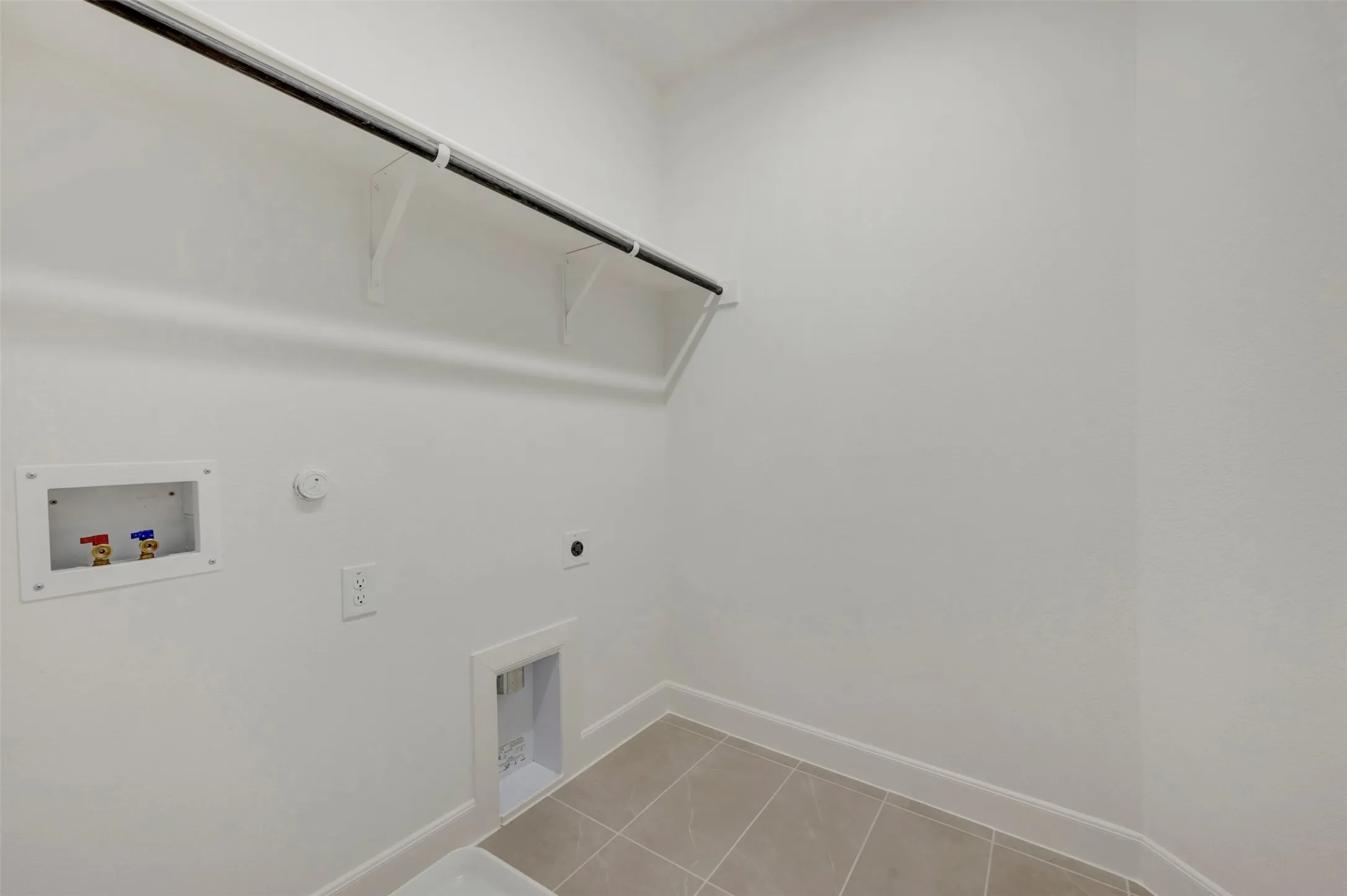Laundry area with neutral wall color, tiled flooring, and a built-in shelf with a hanging rod