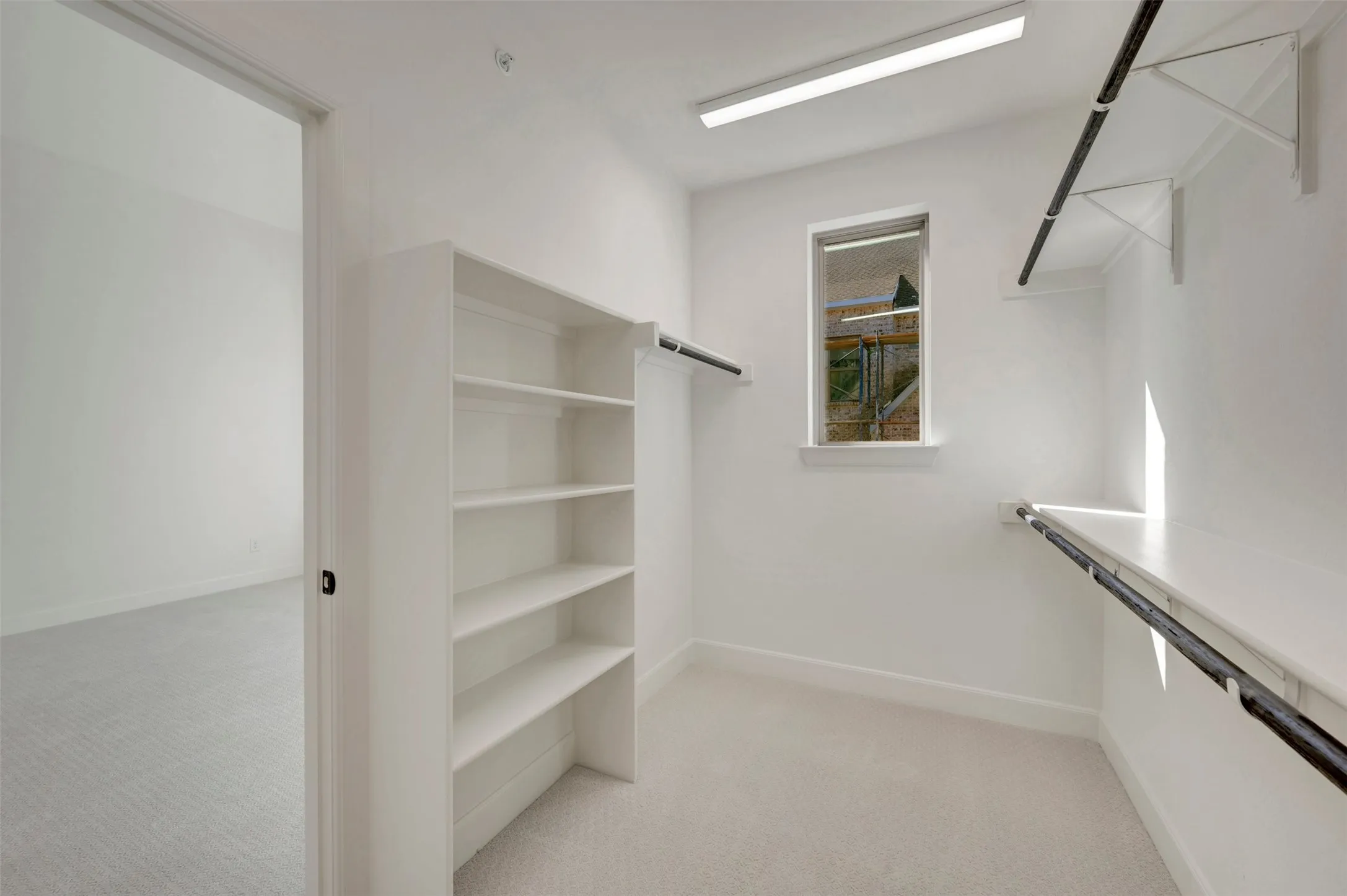 Spacious walk-in closet featuring built-in shelving, hanging rods, and a window for natural light