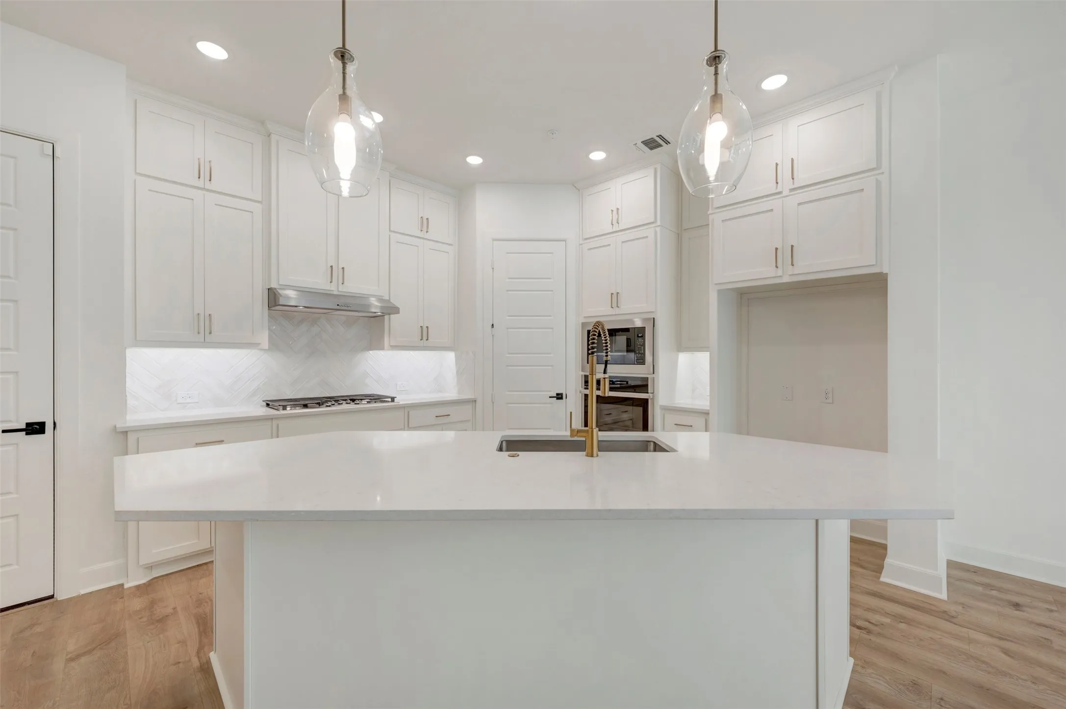 Kitchen featuring a large island with an undermount sink, pendant lighting, white cabinetry, a herringbone tile backsplash, and wood-finish flooring