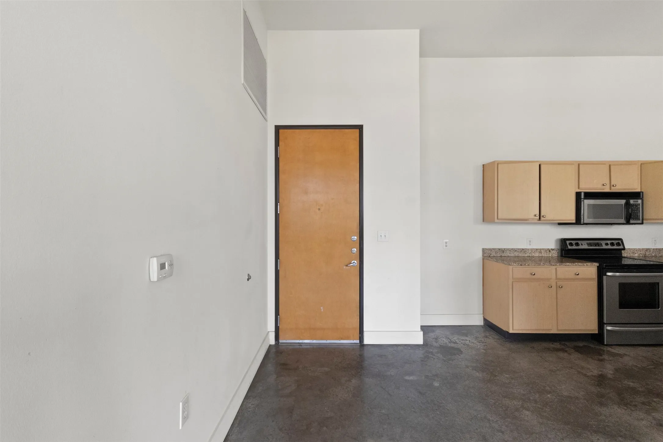 Open-concept space featuring high ceilings, concrete flooring, and a kitchen area